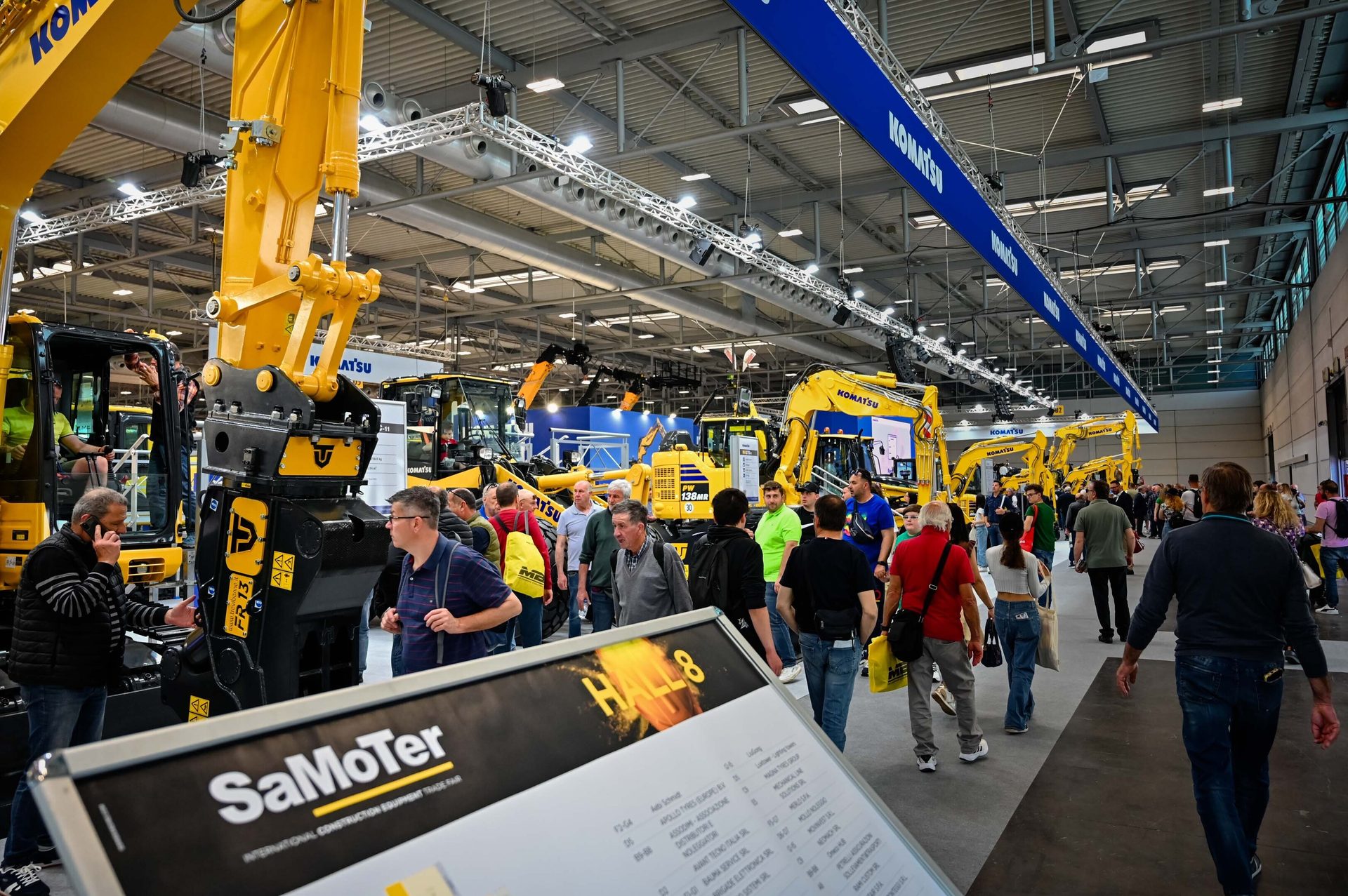 Crowded SaMoTer trade fair with many yellow Komatsu excavators and visitors.