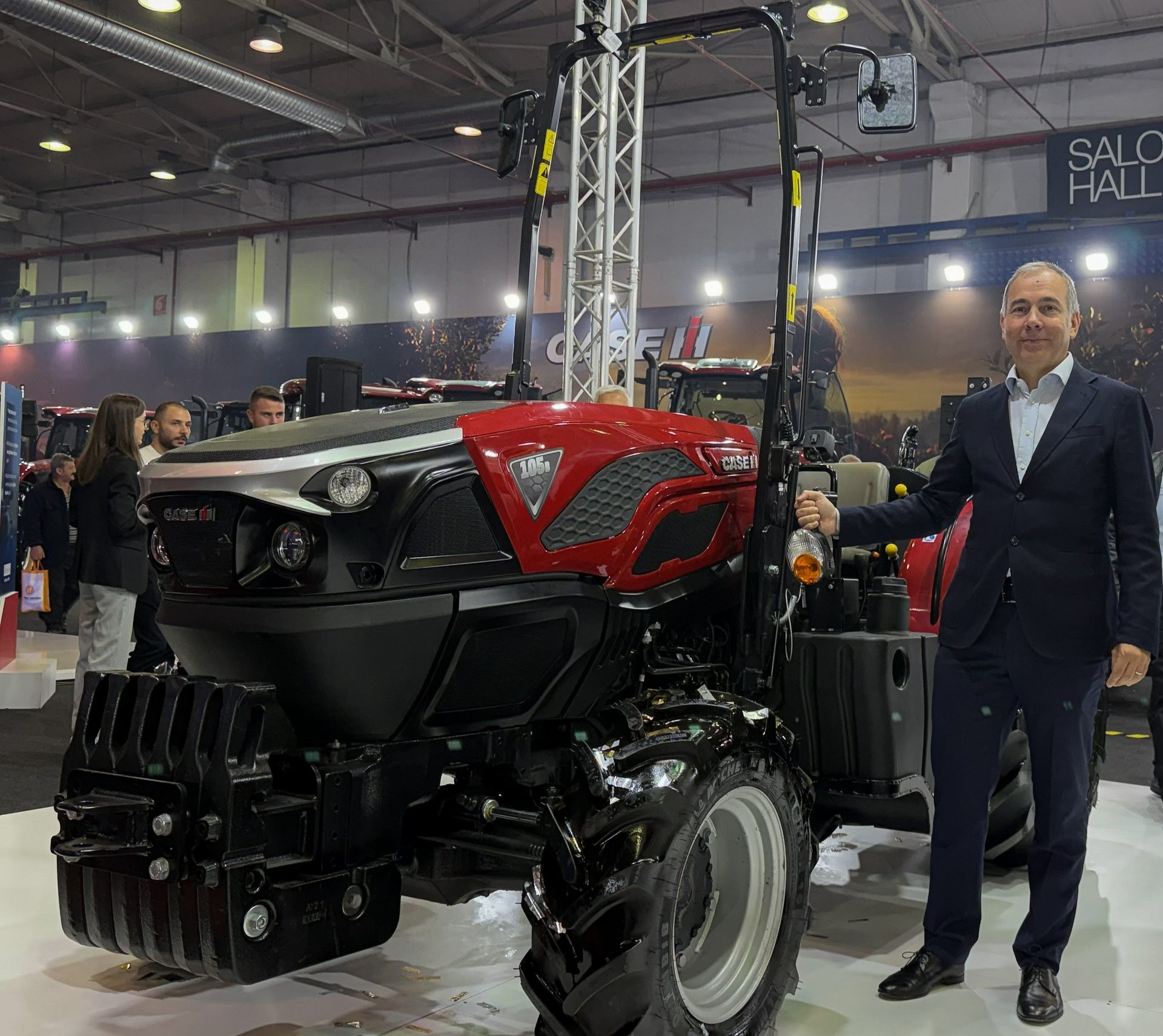 Smiling man next to a red and black Case IH tractor at an indoor show.