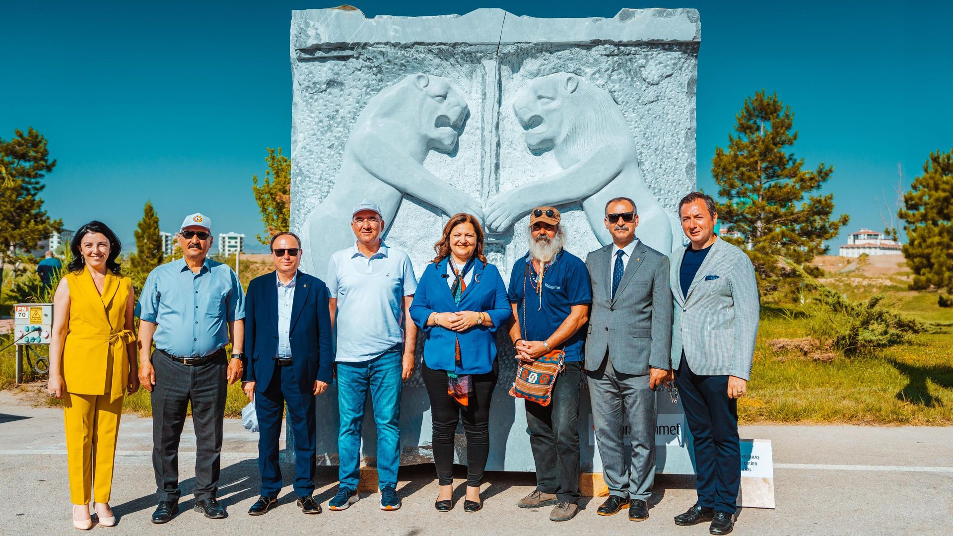 Nine people pose with a large stone sculpture depicting two roaring lions.