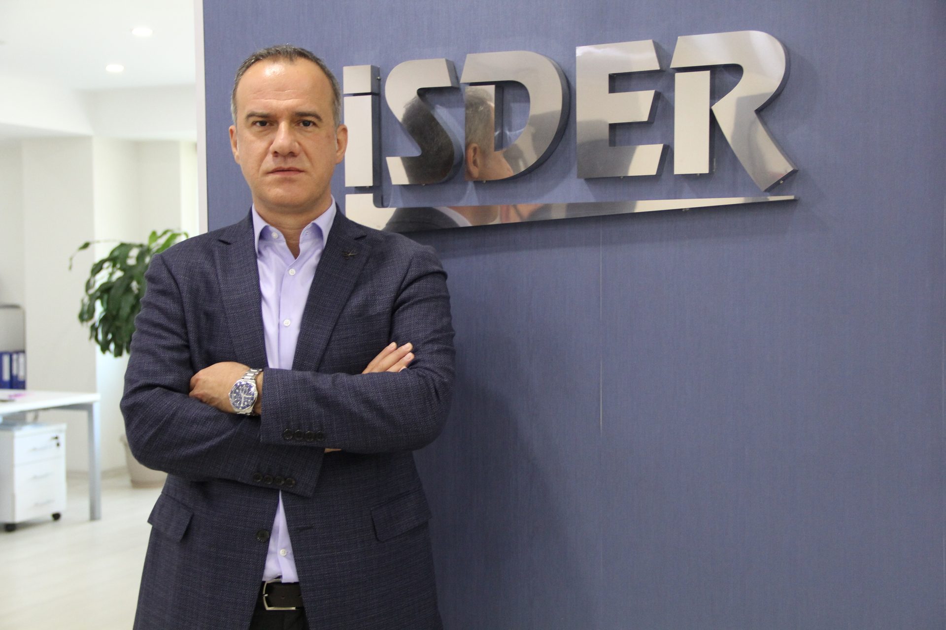 Man with crossed arms in front of ISDER logo on a blue wall.