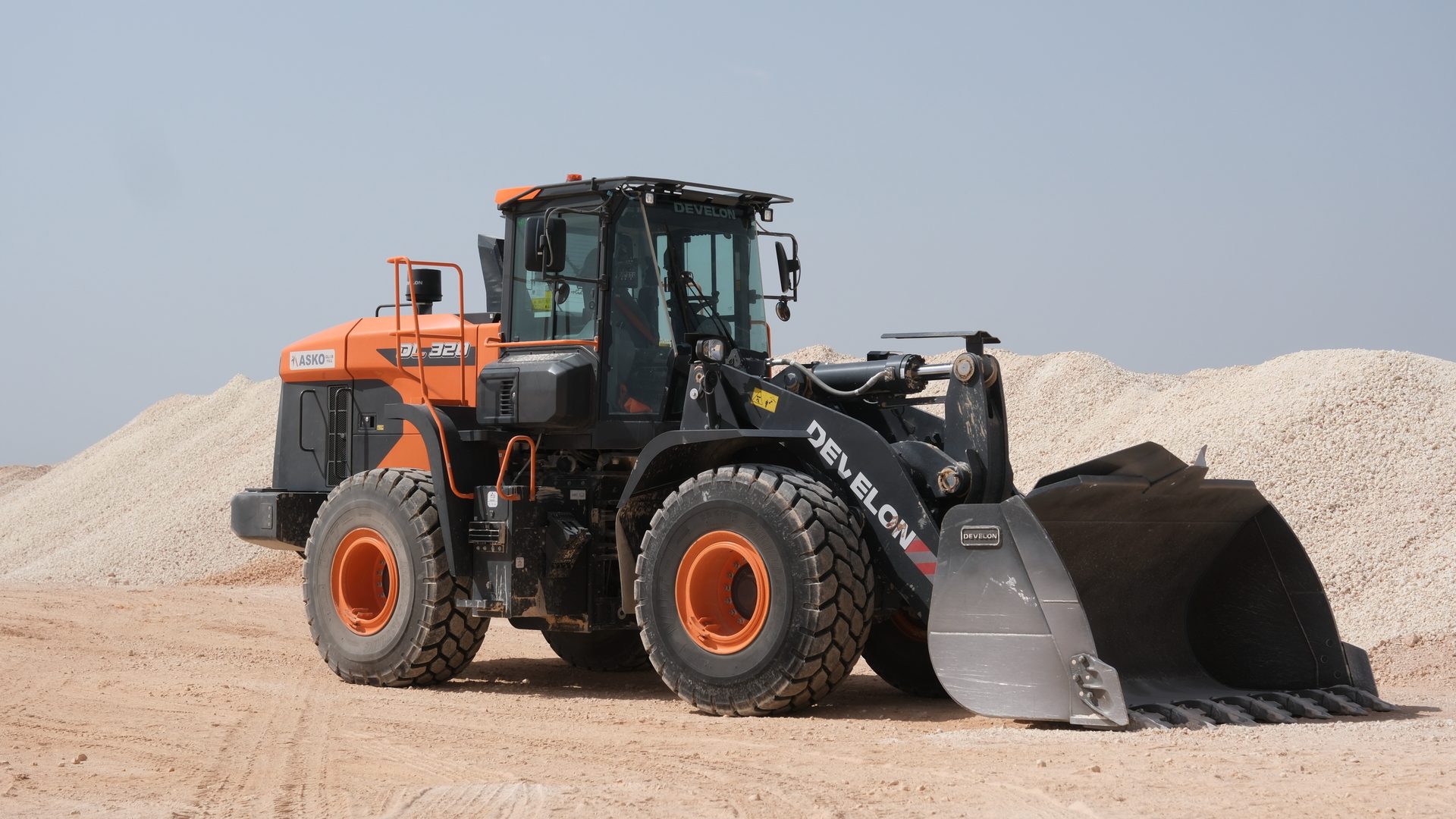 Orange and black Develon wheel loader parked on dirt with gravel piles.