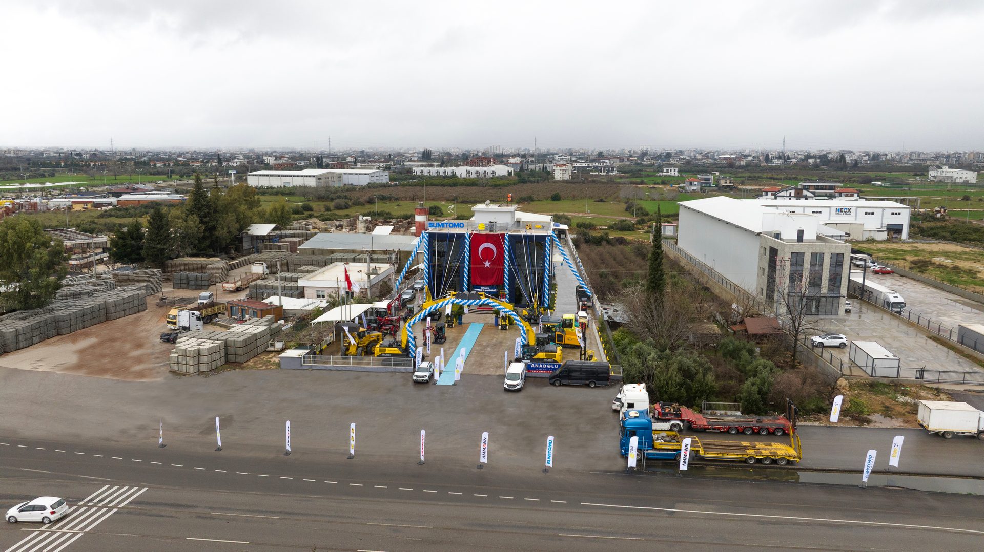 Aerial view of Sumitomo construction equipment display with a large Turkish flag under cloudy skies.