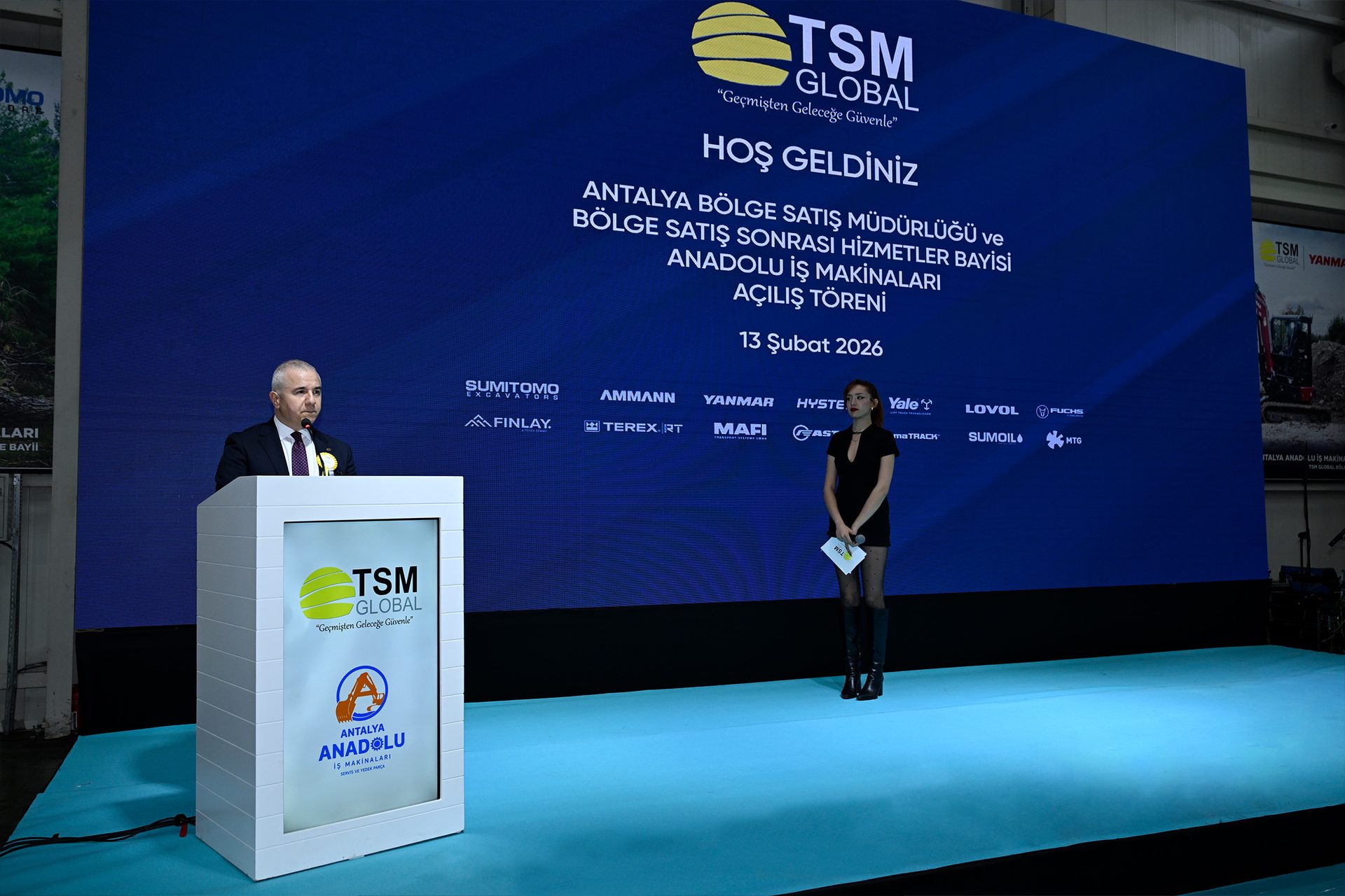 Opening ceremony for an industrial machinery sales and service center, with speakers on stage and a large display.