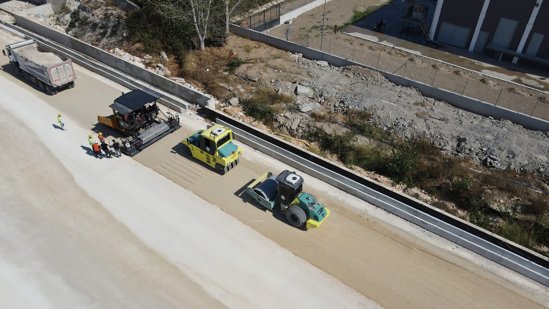 Aerial view of a road construction site with a paver, two rollers, and workers.