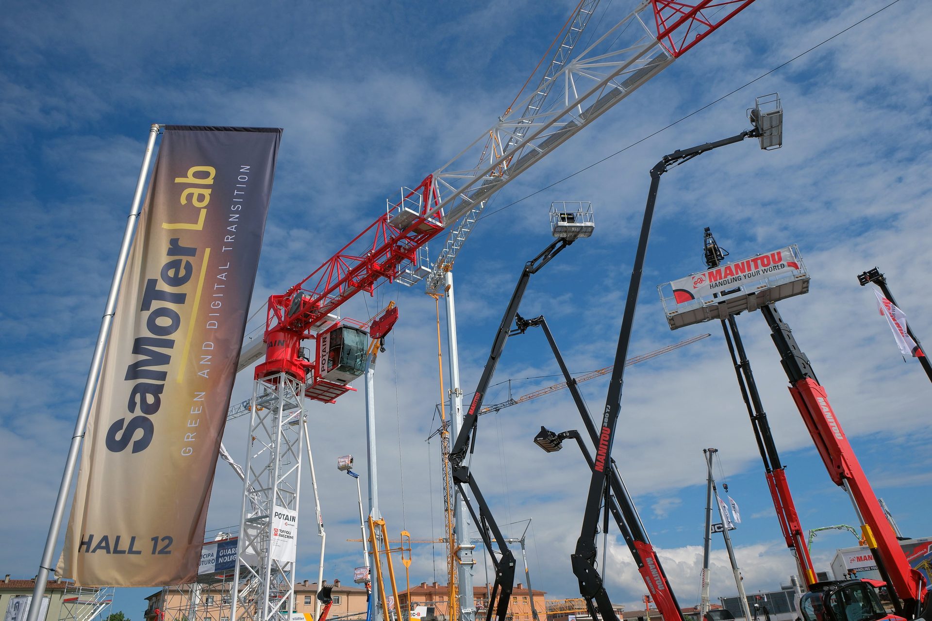 Low-angle shot of construction cranes and aerial platforms at an exhibition under a blue sky.
