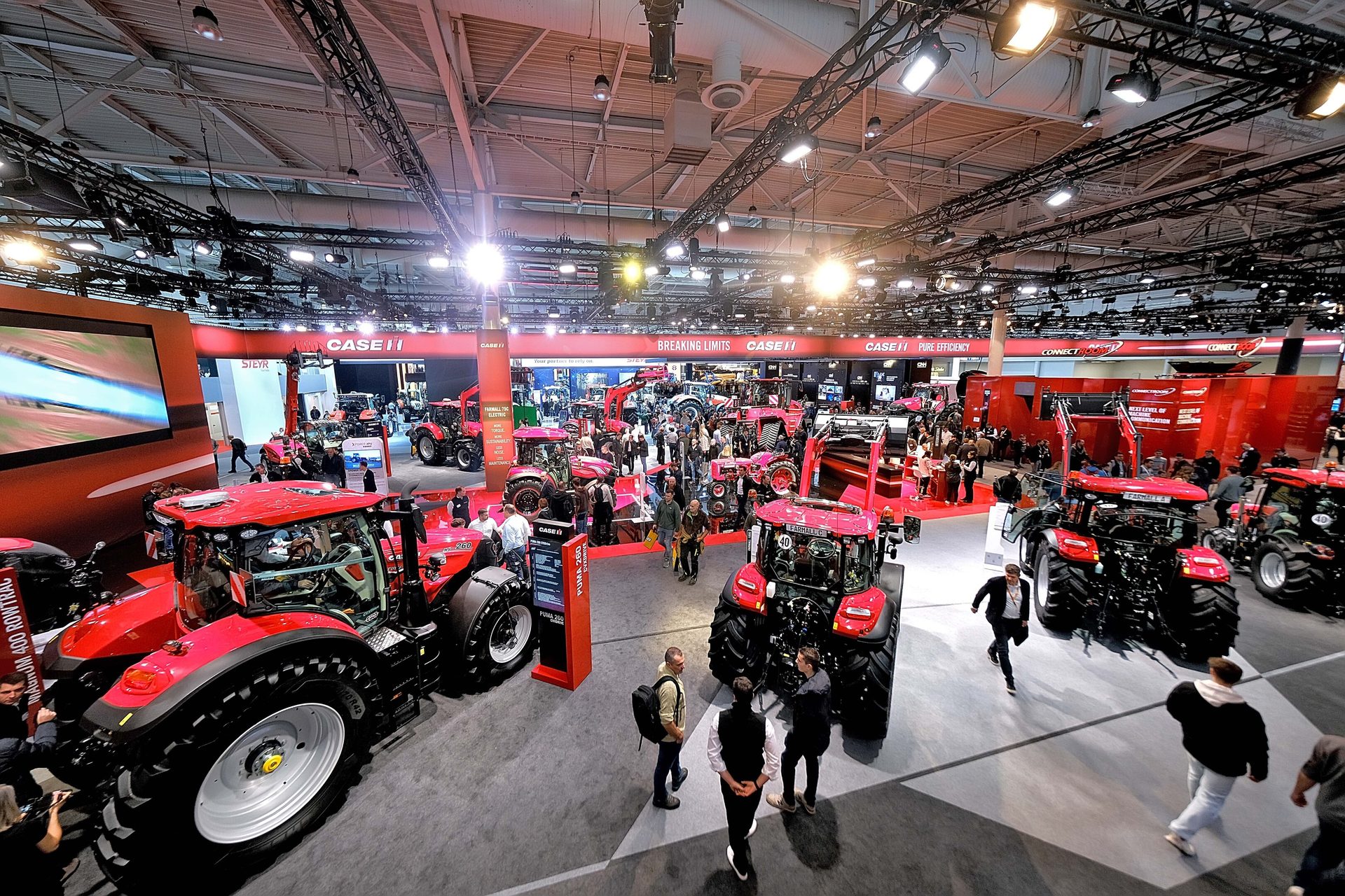 Busy indoor agricultural trade show with numerous red Case IH tractors and people.