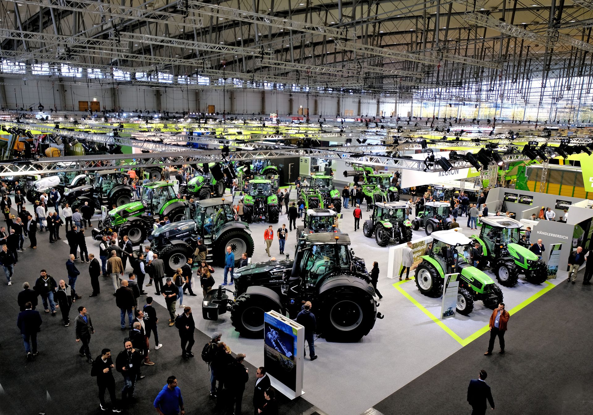 Large agricultural trade show floor with many green tractors and attendees.