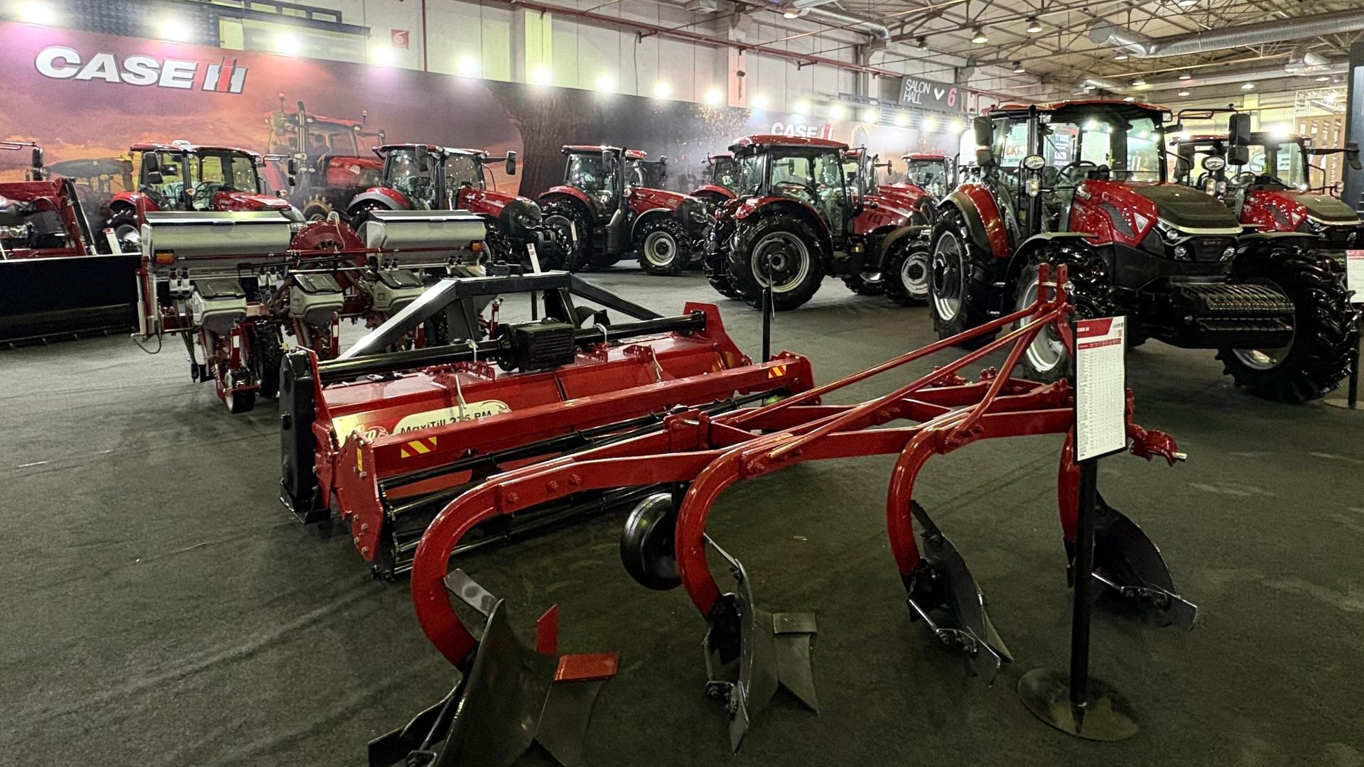 Case IH agricultural exhibit with red tractors, tillers, and plows indoors.