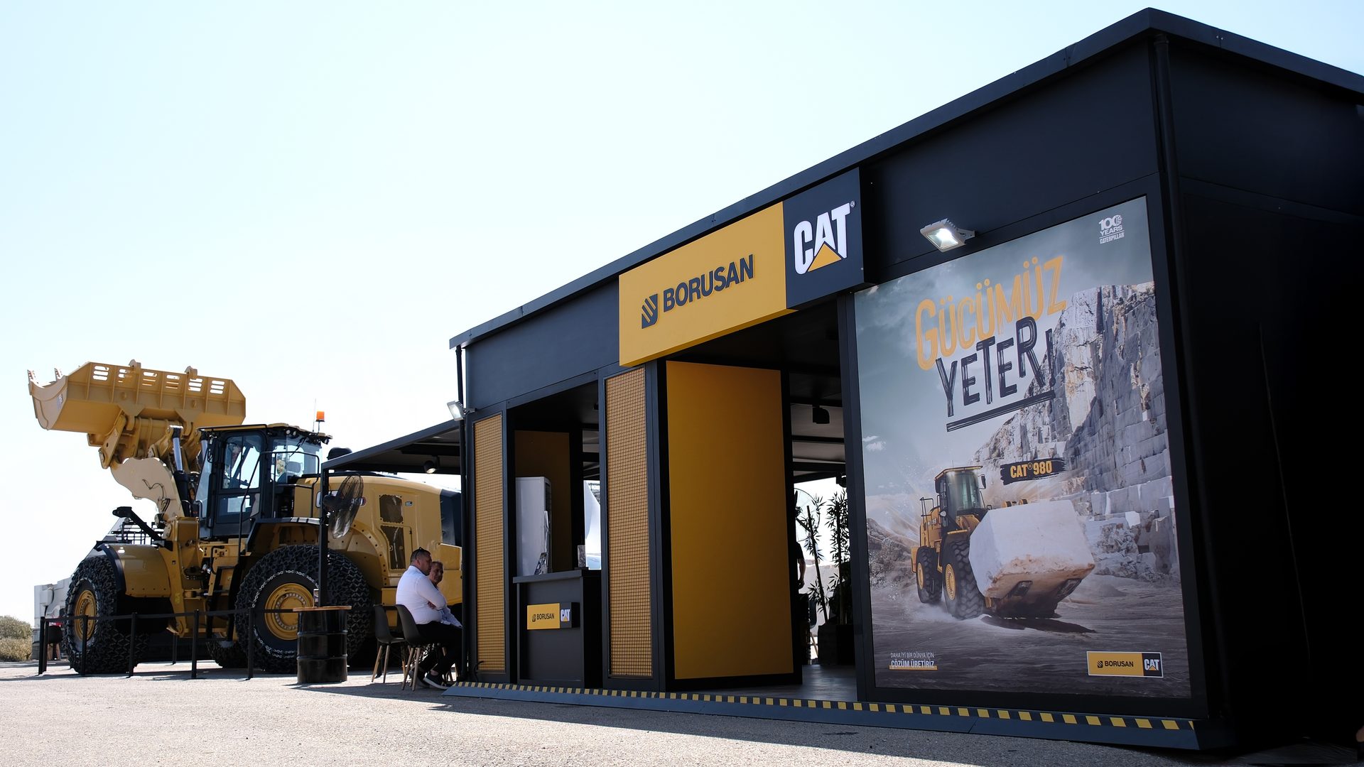 A large yellow Cat wheel loader is displayed next to a Borusan Cat branded booth with a poster.