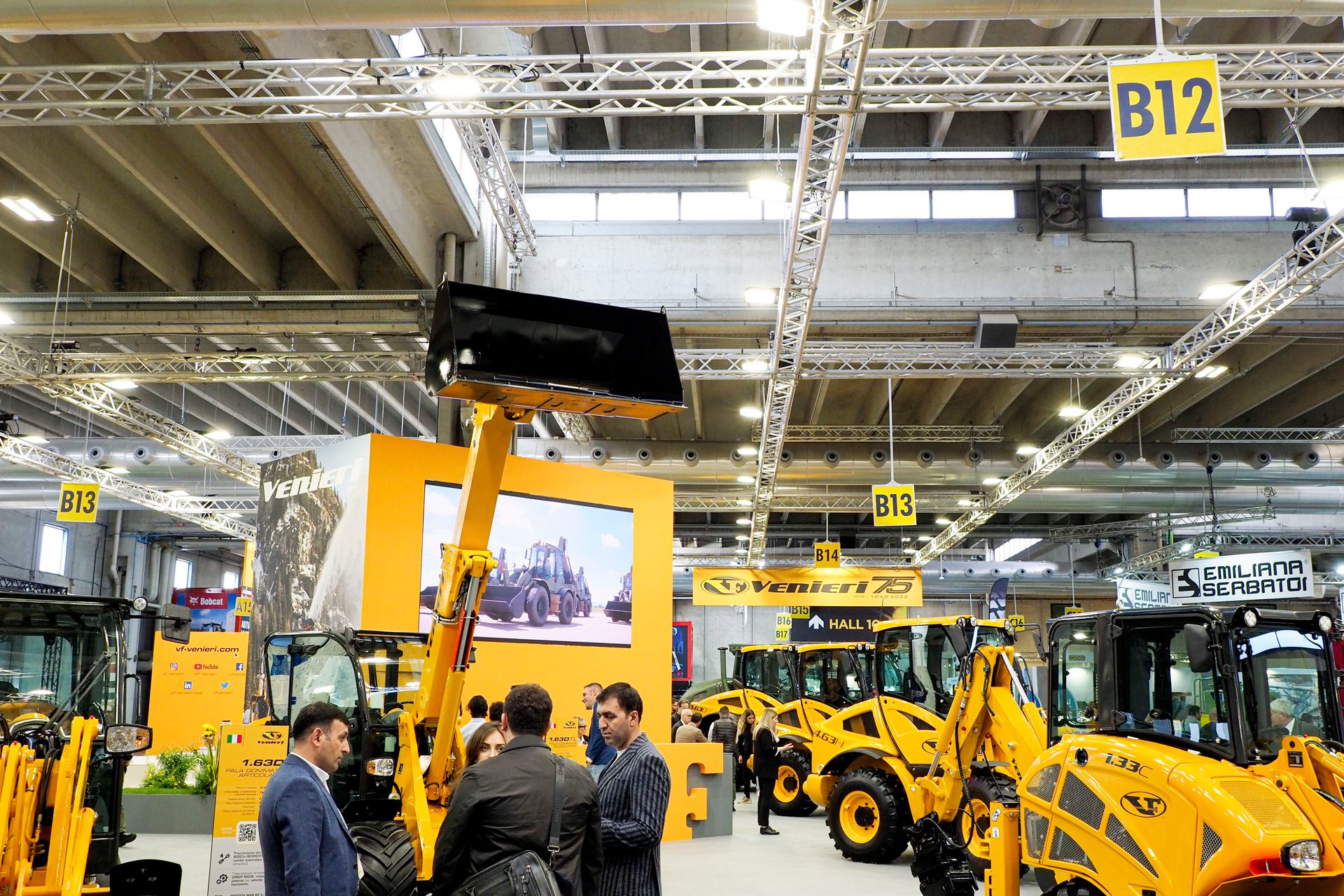 Indoor trade show with yellow Venieri construction machinery and visitors.