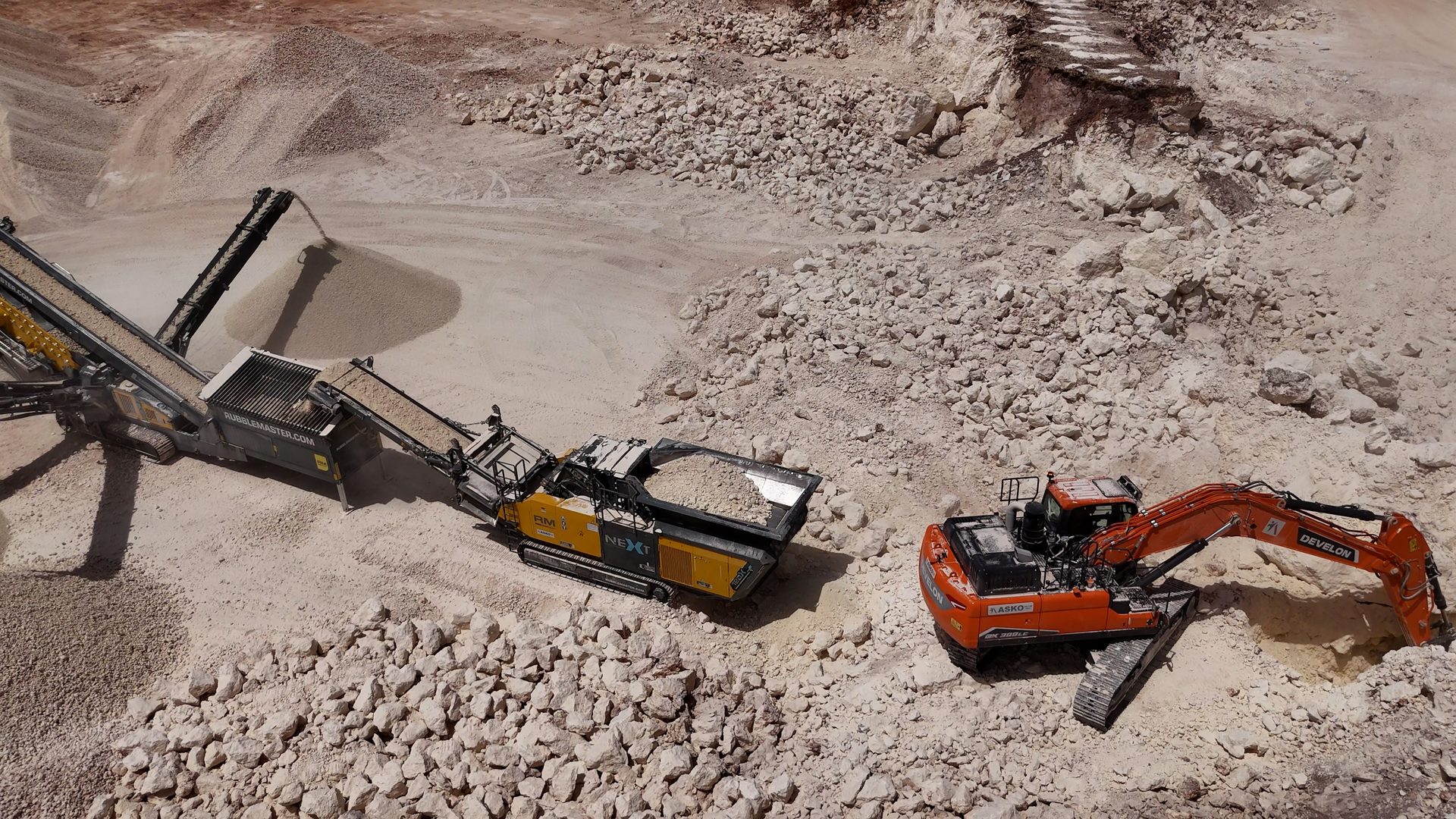 Crusher and excavator processing rock in a bright quarry.