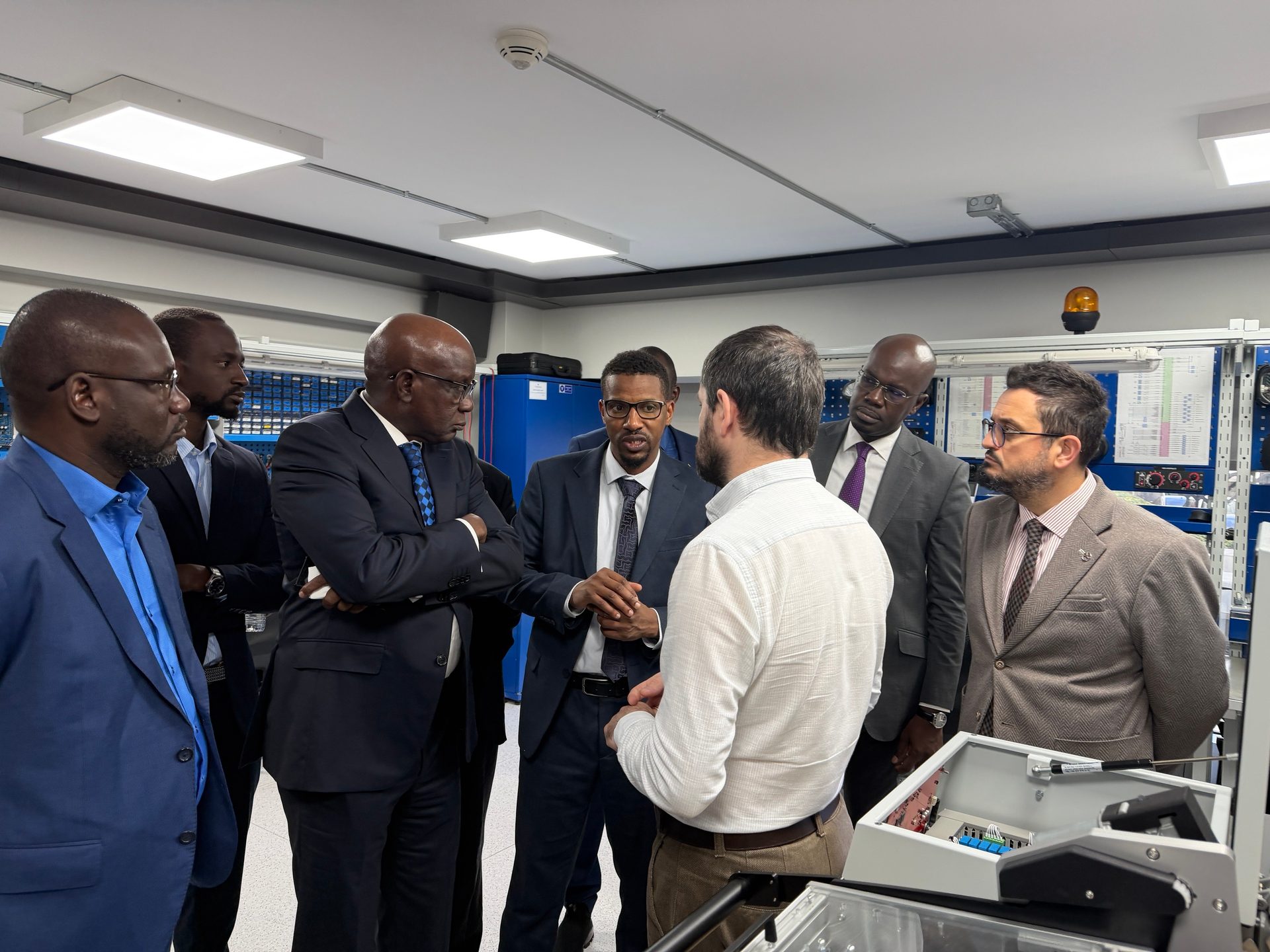 Group of men, mostly in suits, discussing equipment in a modern lab setting.