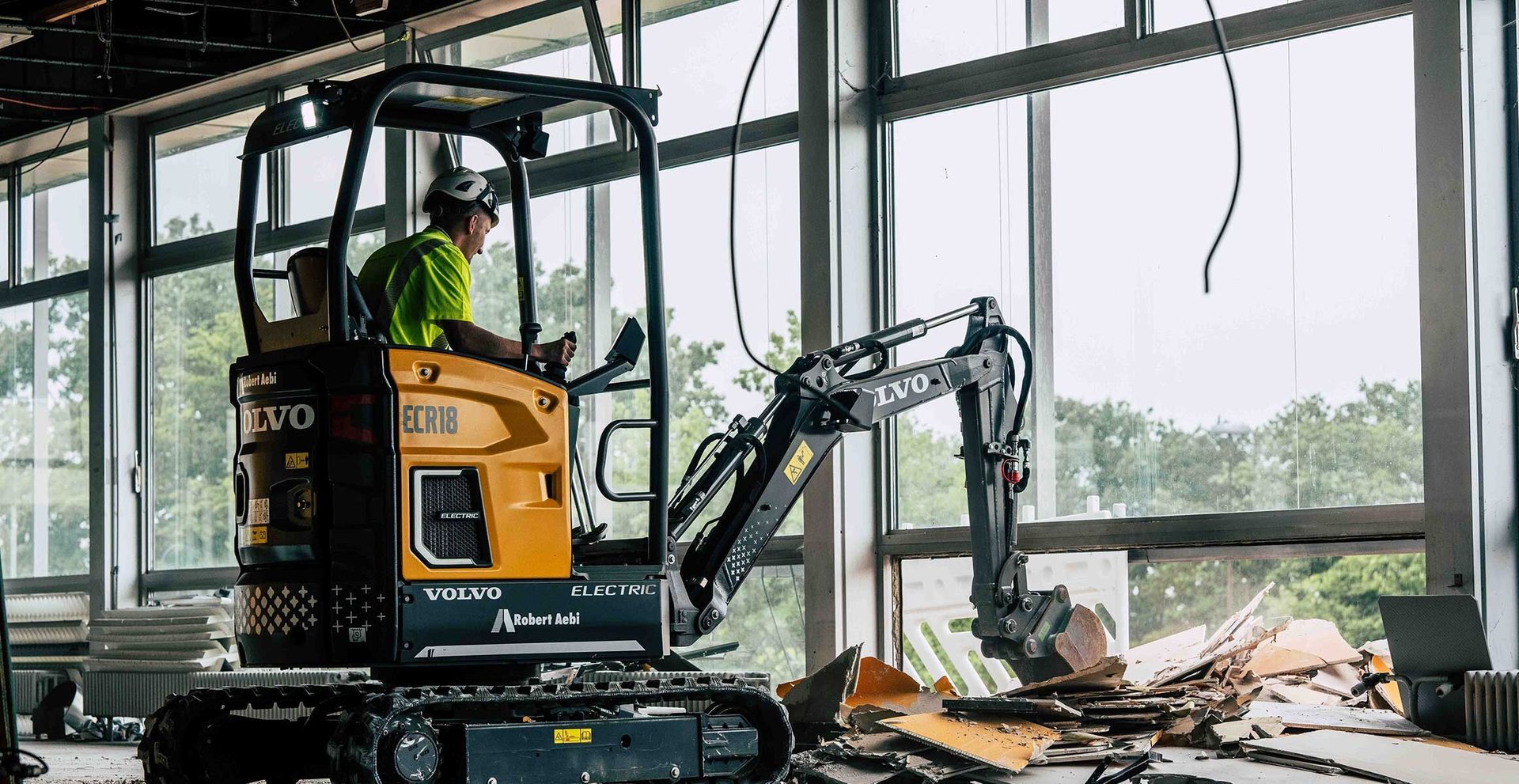 An operator in a Volvo ECR18 electric mini excavator demolishing an interior space with debris.