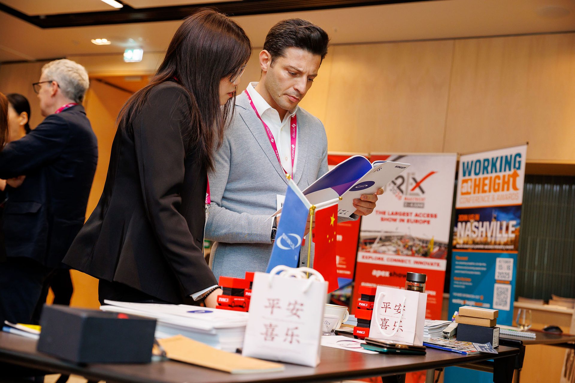 Two attendees at an event review a brochure together at a display table with promotional items.