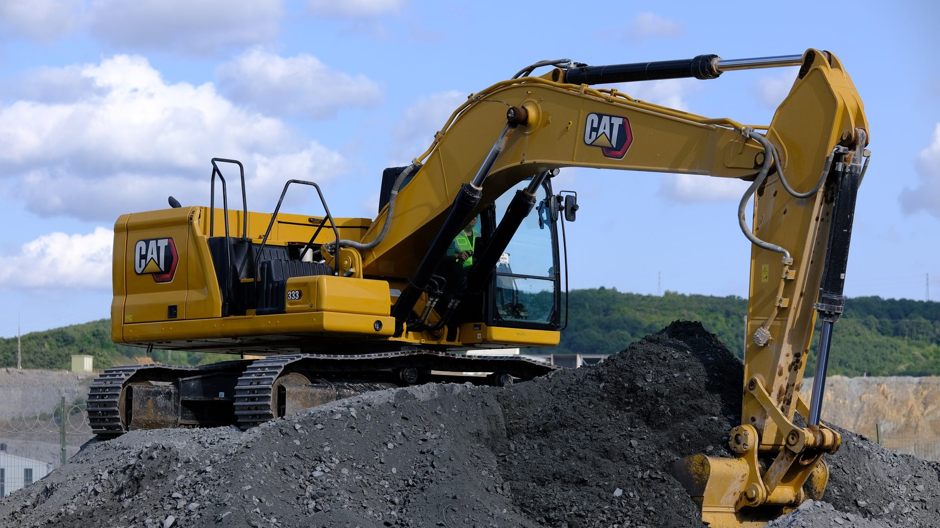 Yellow Caterpillar 333 excavator on a gravel pile under a blue sky.