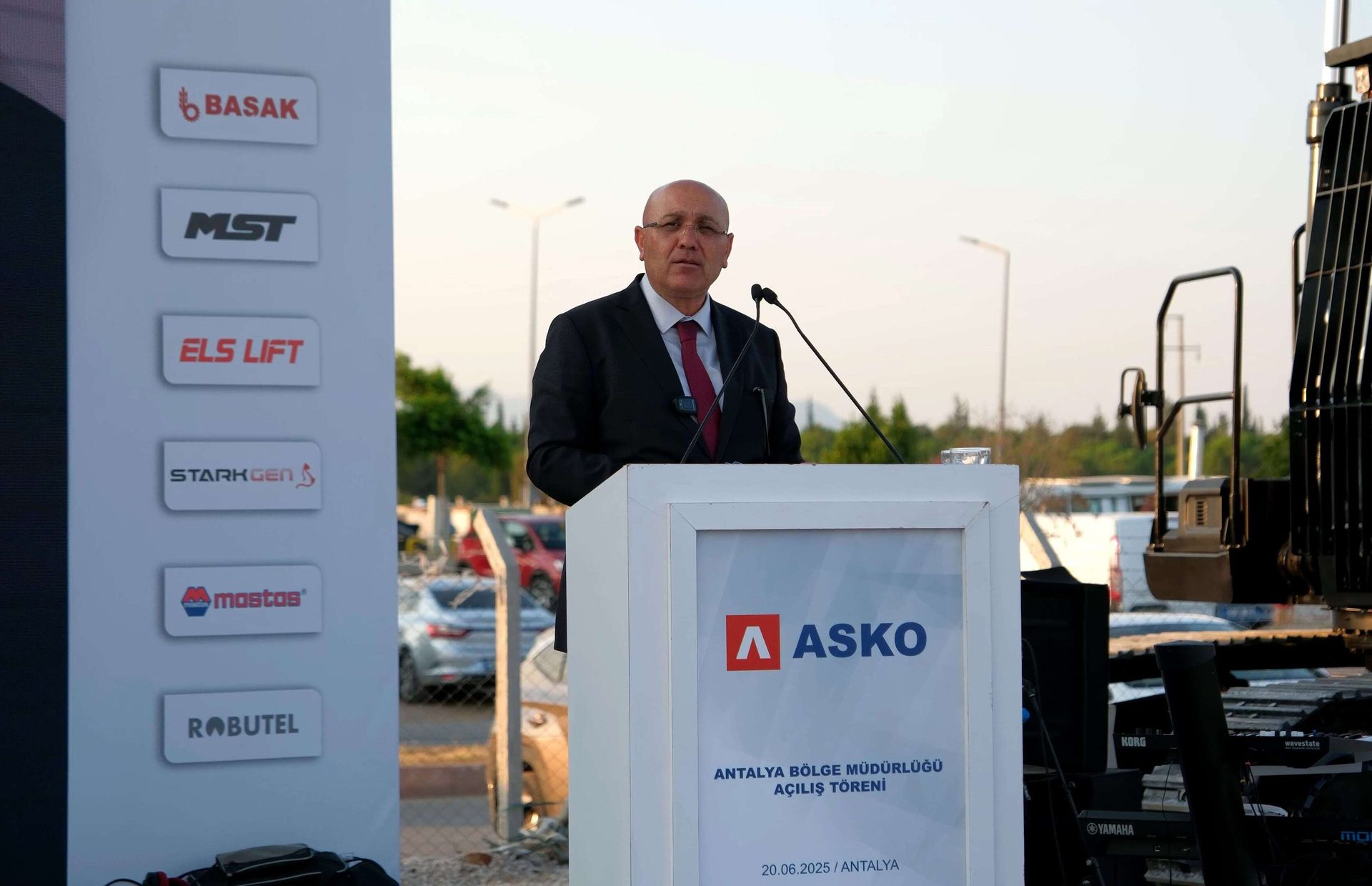 Man at podium for ASKO Antalya opening ceremony, with sponsor logos displayed.