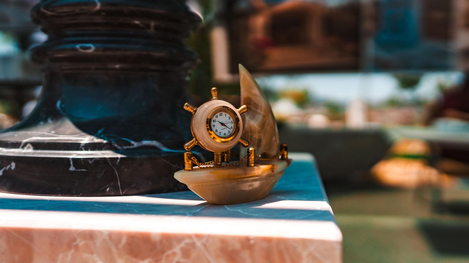 Boat-shaped stone clock with a gold ship's wheel face on marble.