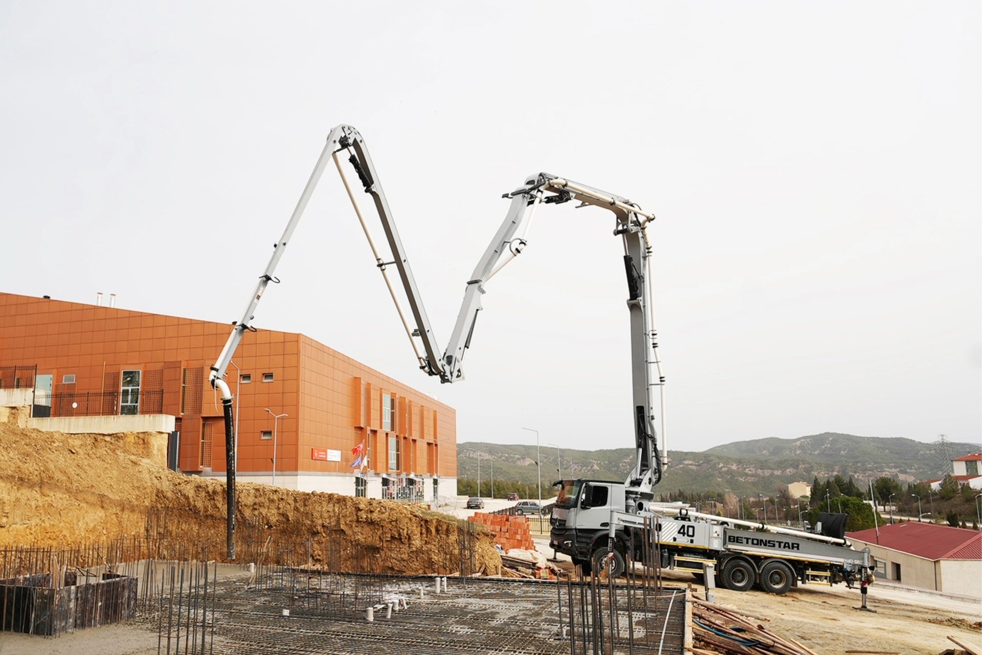 A concrete pump truck with an extended boom pours concrete into a rebar foundation at a construction site.