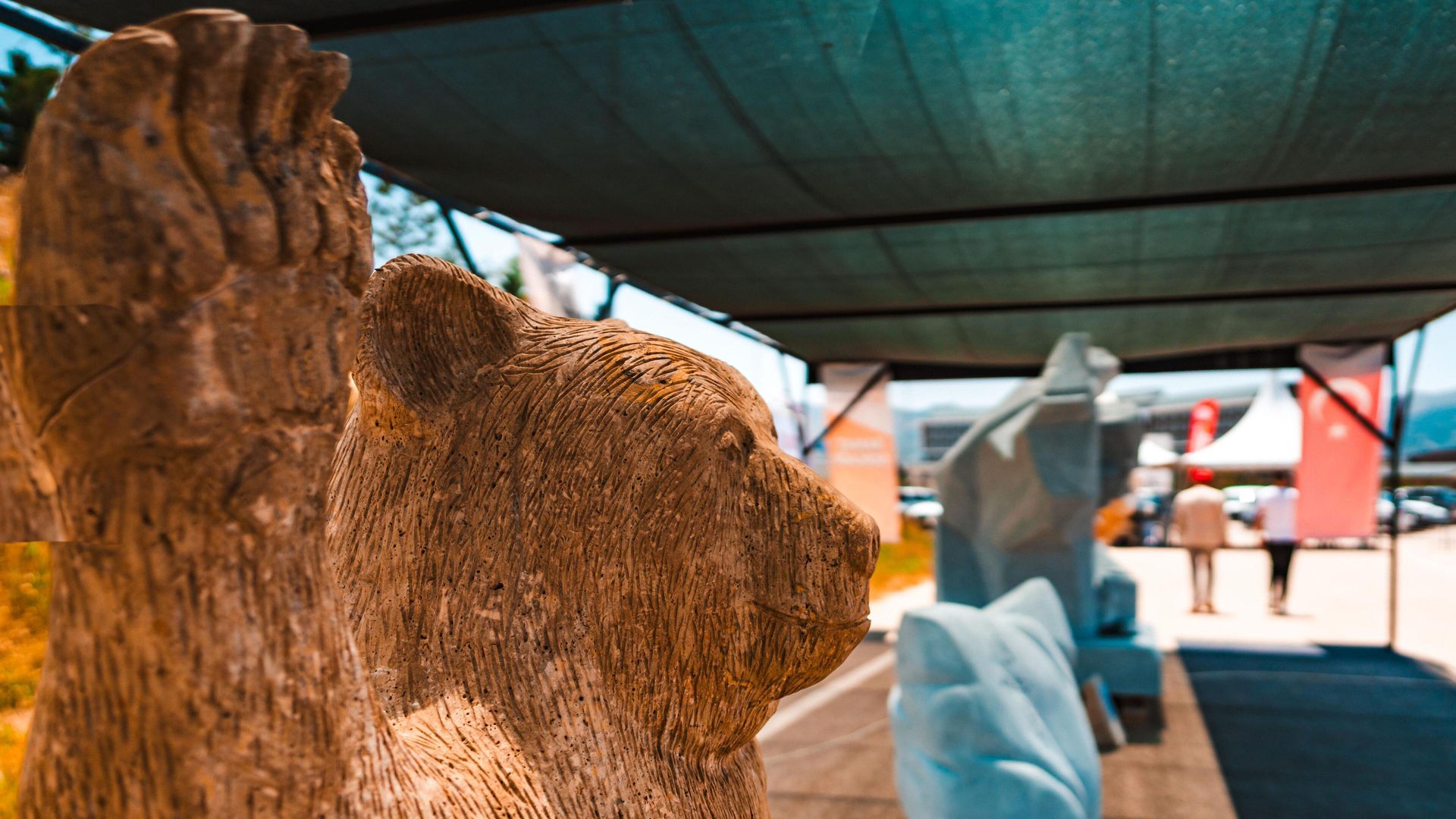 Textured animal statue with blurred background of people, tents, and a canopy.