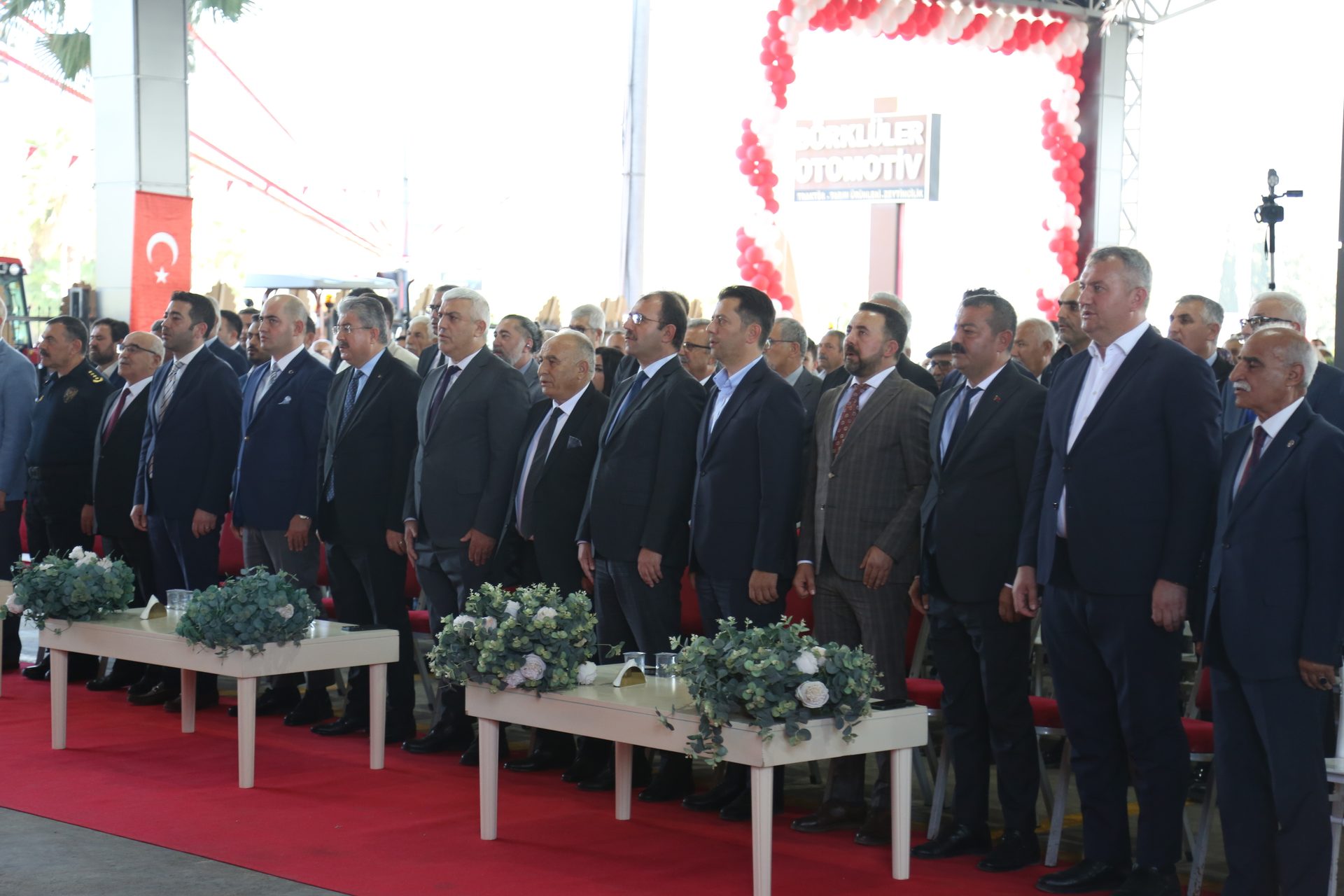 Formal event with men in suits standing on a red carpet, Turkish flag in background.