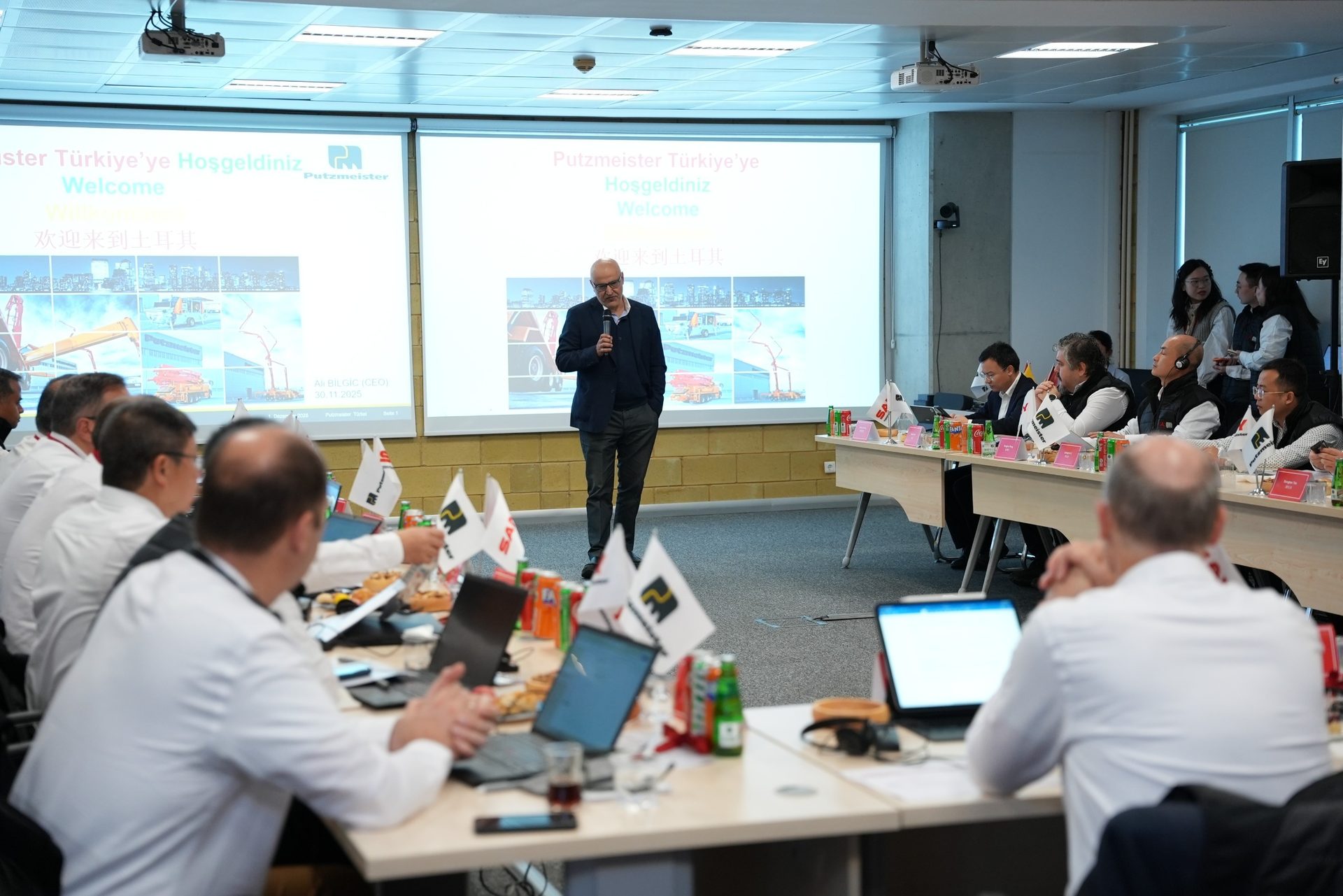 A man presents to an audience at a business meeting, with a "Welcome to Putzmeister Turkey" screen behind him.