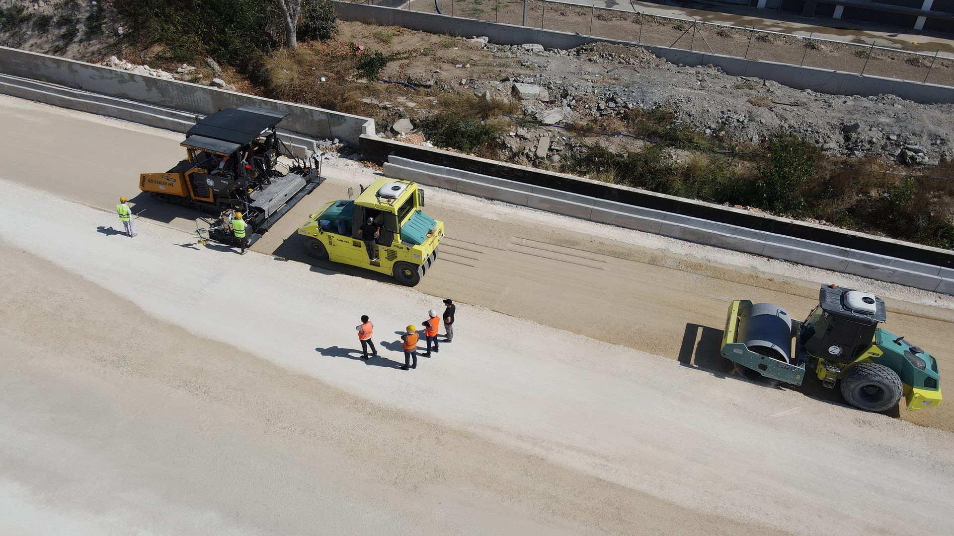 Aerial view of road construction with paver, rollers, and workers.