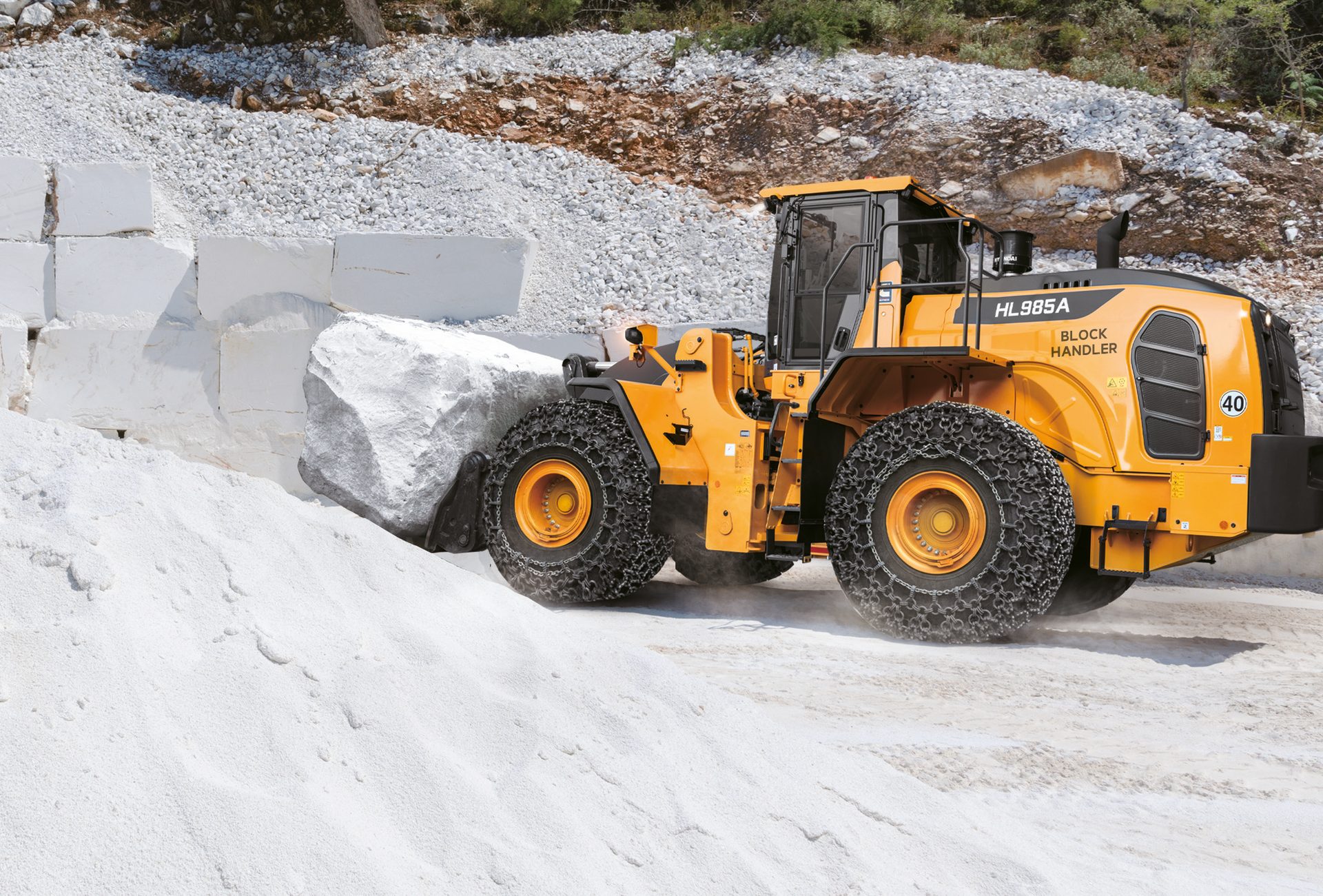 Yellow block handler loader with tire chains pushing a large white stone in a quarry.