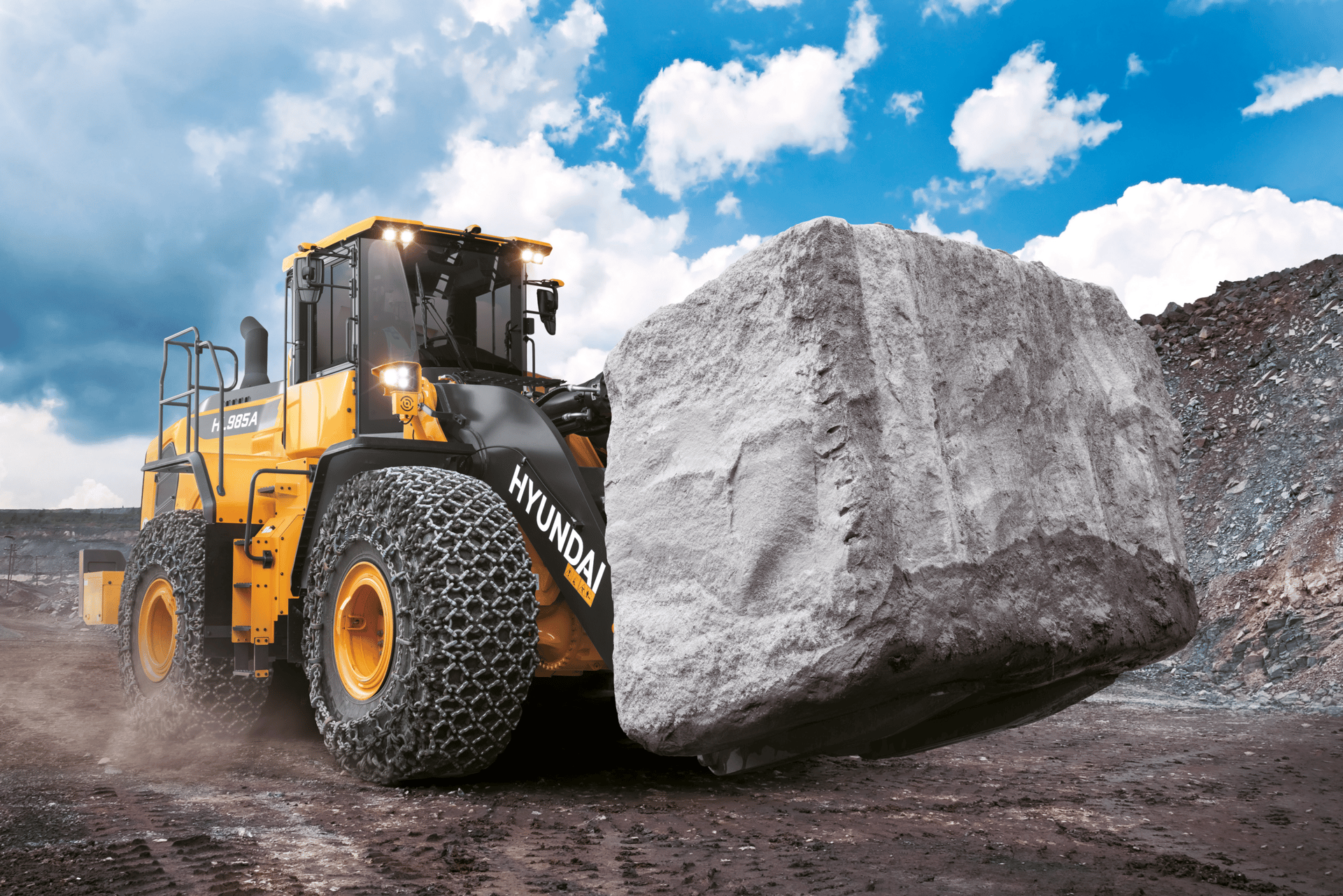Yellow Hyundai wheel loader transporting a massive rock at a quarry.