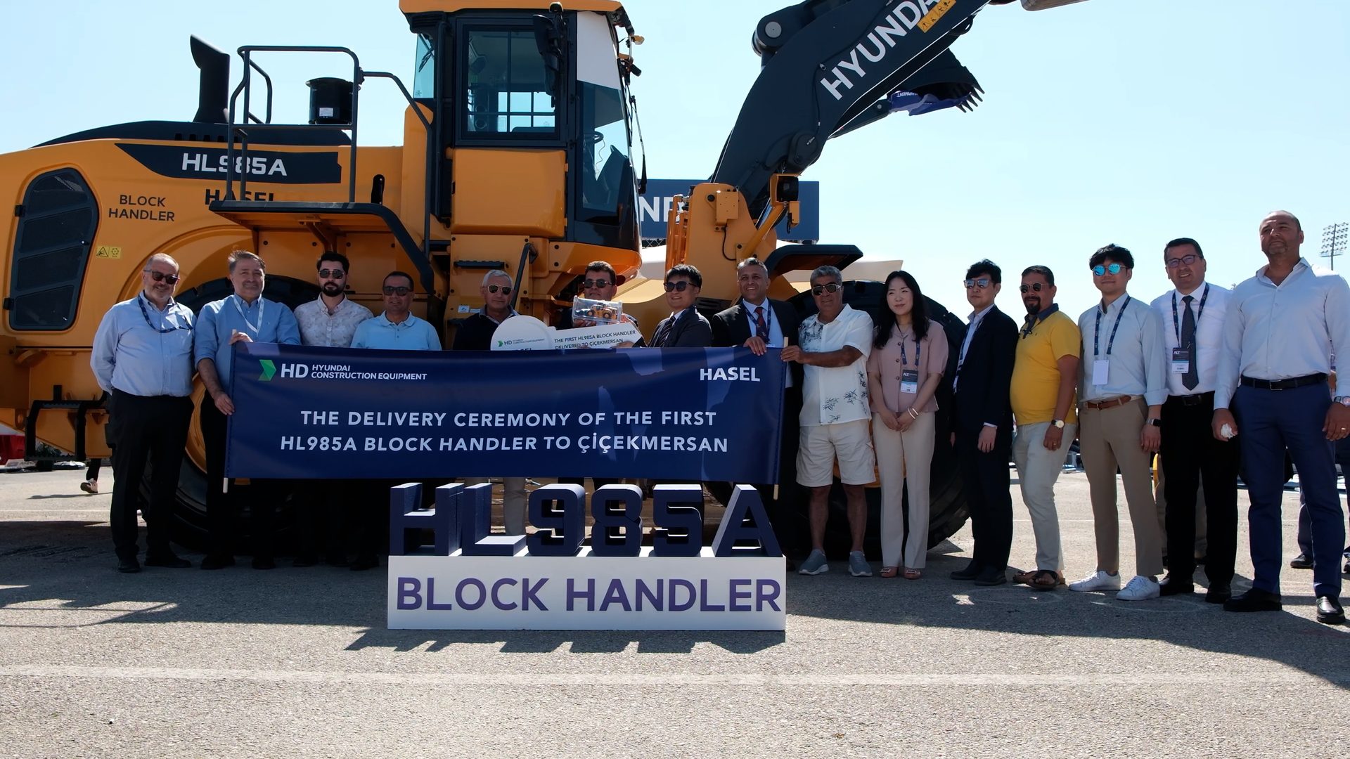 Delivery ceremony of a Hyundai HL985A Block Handler with a group of people and a banner.