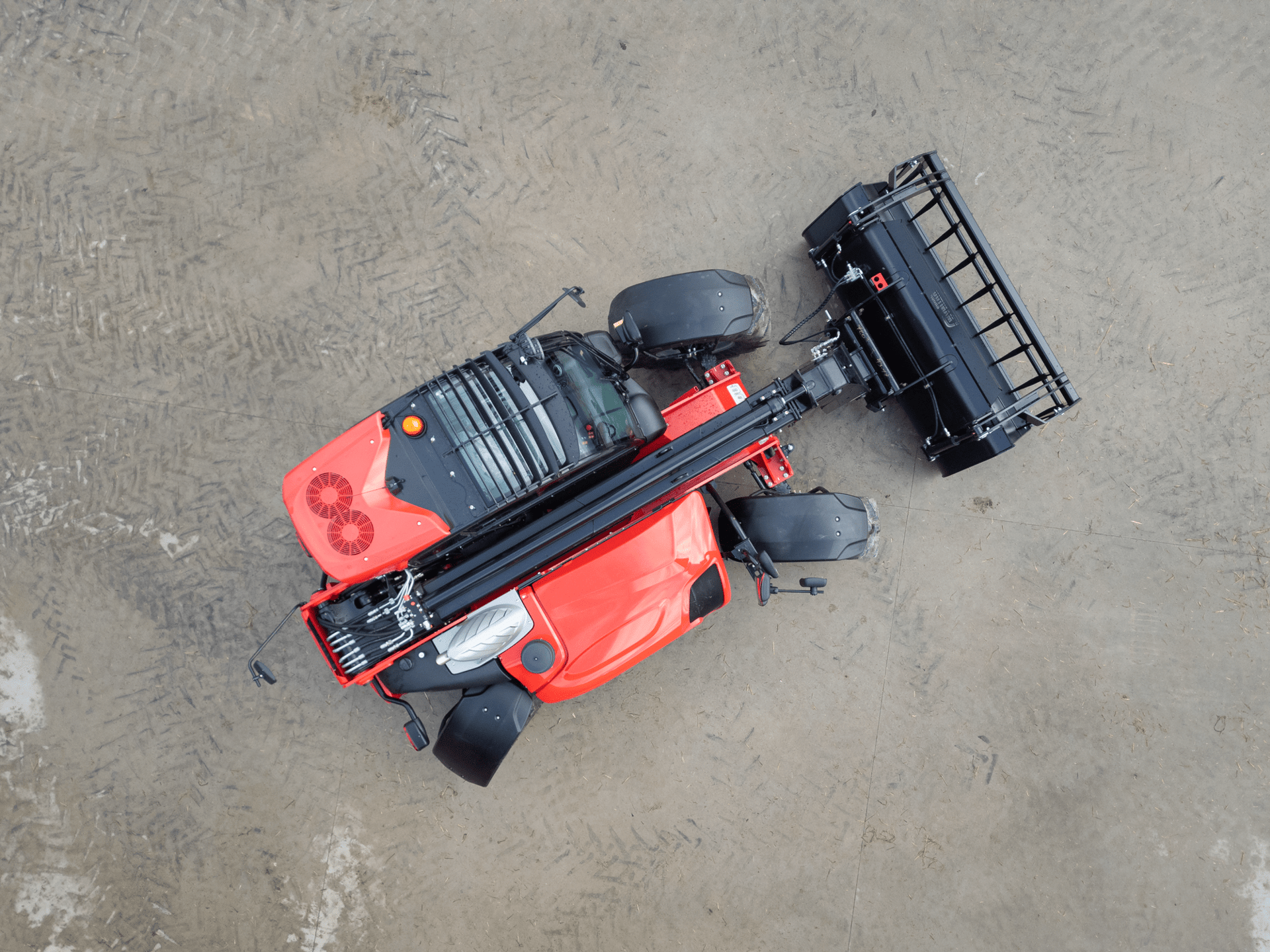 Overhead view of a red agricultural machine with a black attachment on dirt.