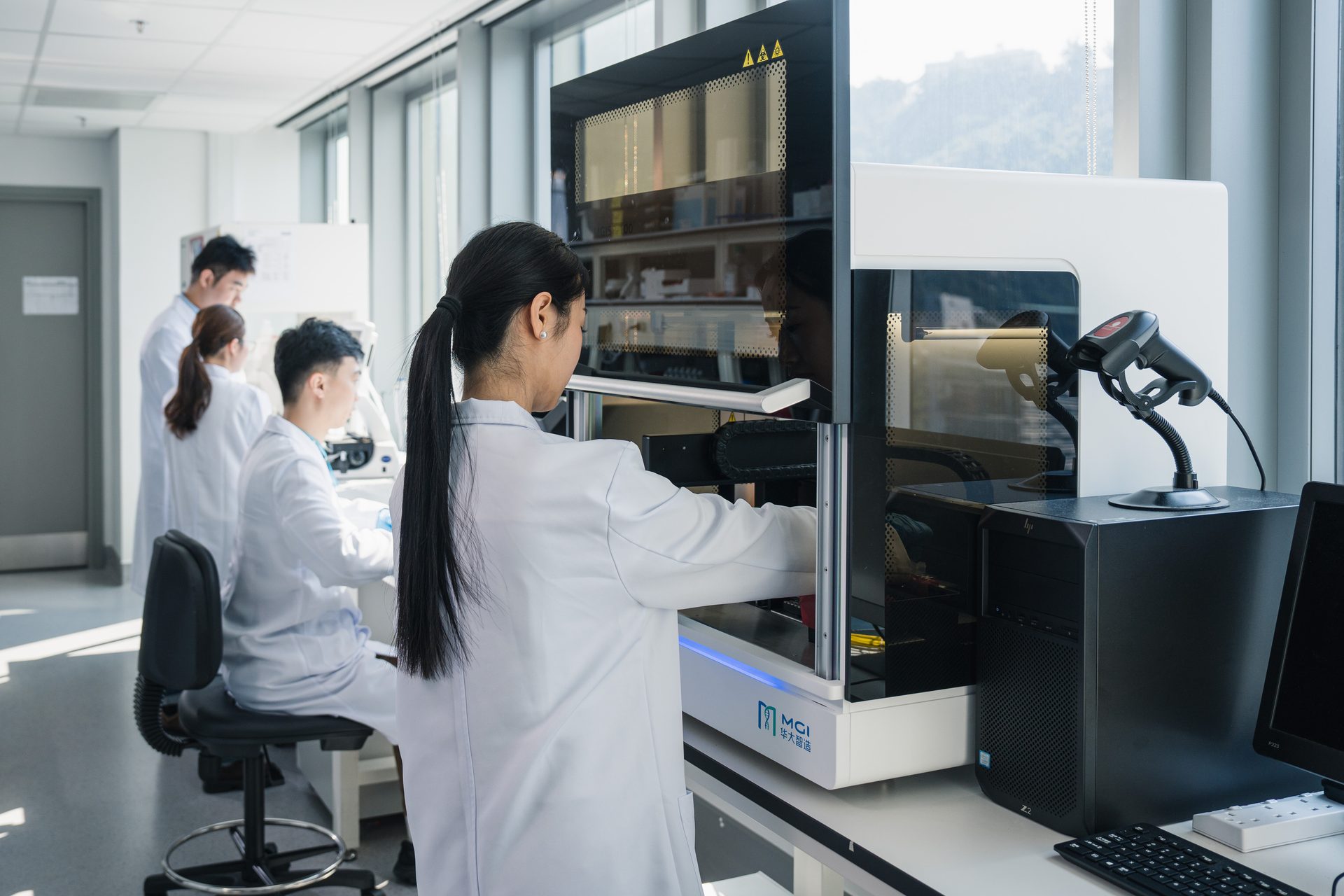 Scientists in lab coats using MGI lab equipment and computers in a modern research facility.