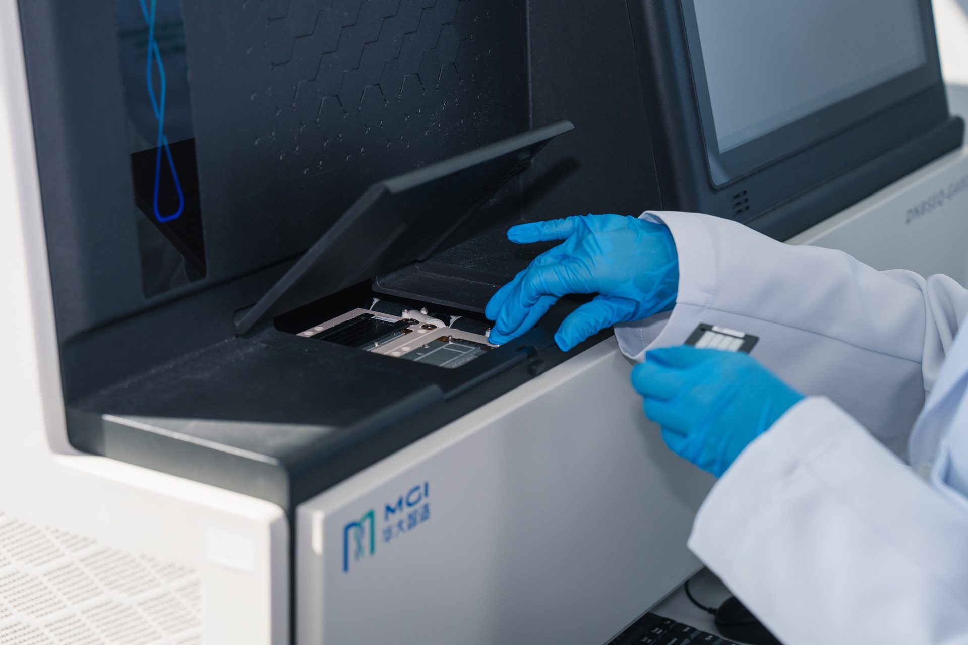 A scientist in blue gloves places a sample into an MGI DNA sequencing machine.