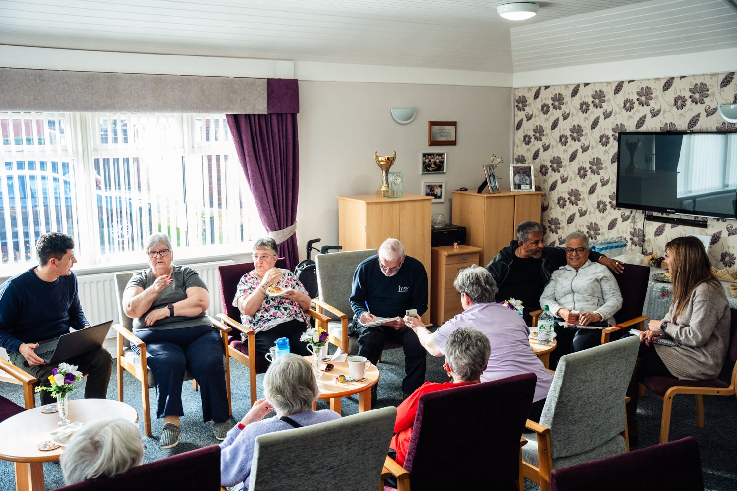 Photos of nibbles and natter event, MSV residents sit around a table with food and drink. MSV staff member taking notes