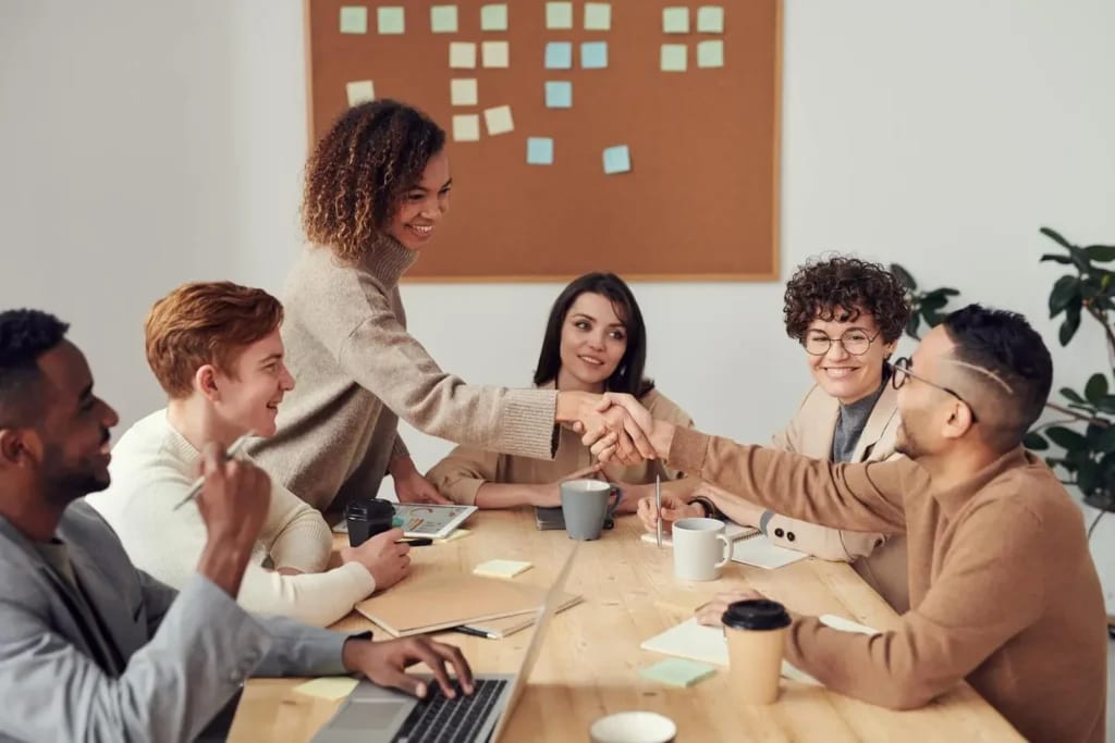 Smiling colleagues shaking hands at a diverse team meeting.