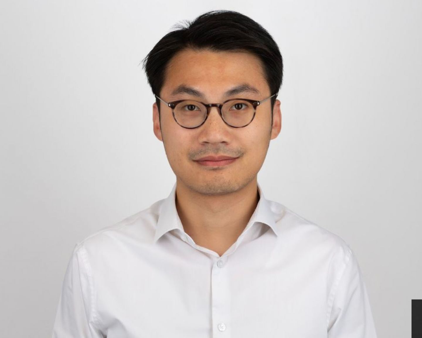 Headshot of a man in glasses and a white shirt against a white background.