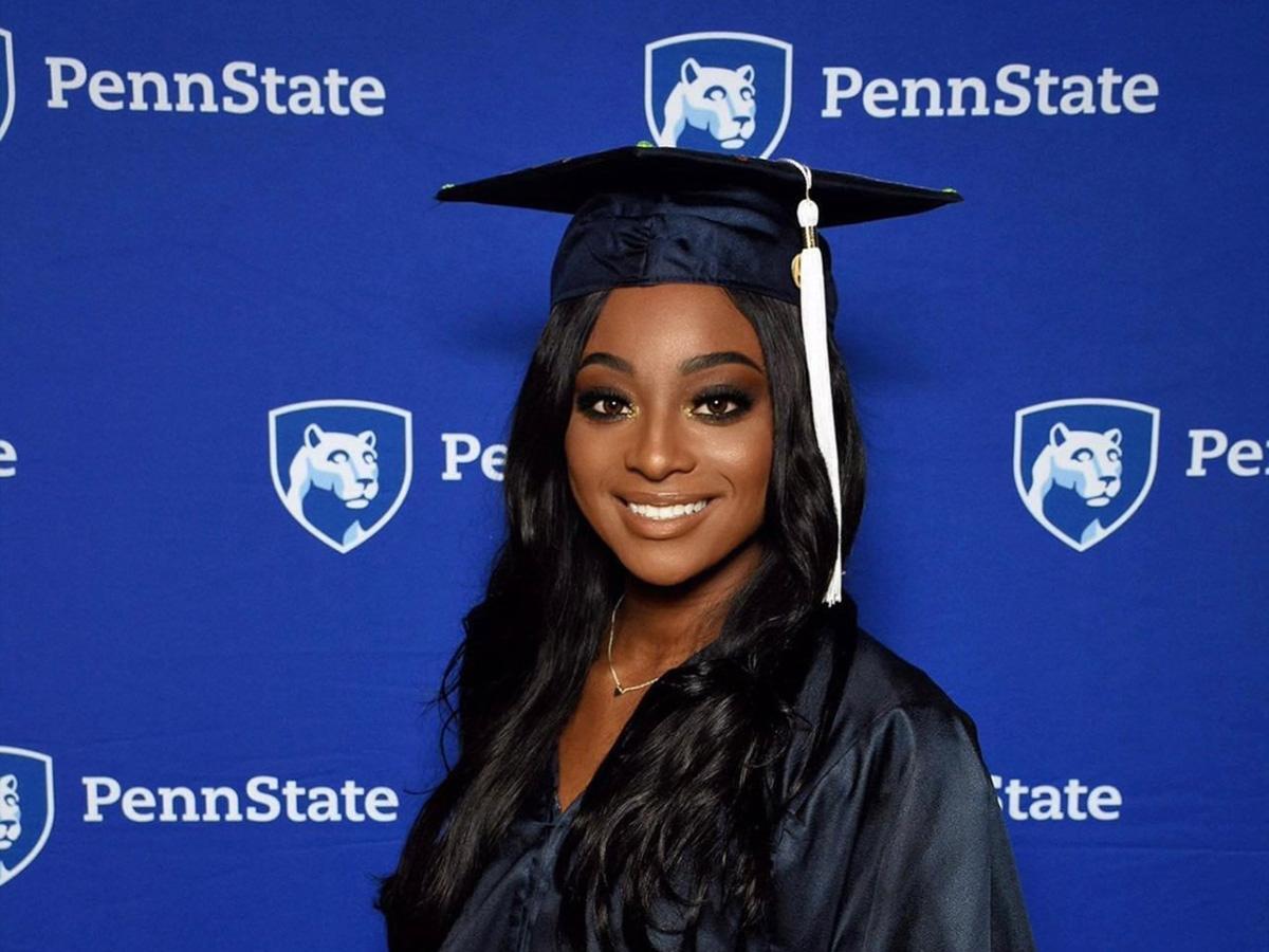 Smiling woman in graduation cap and gown against a Penn State backdrop.