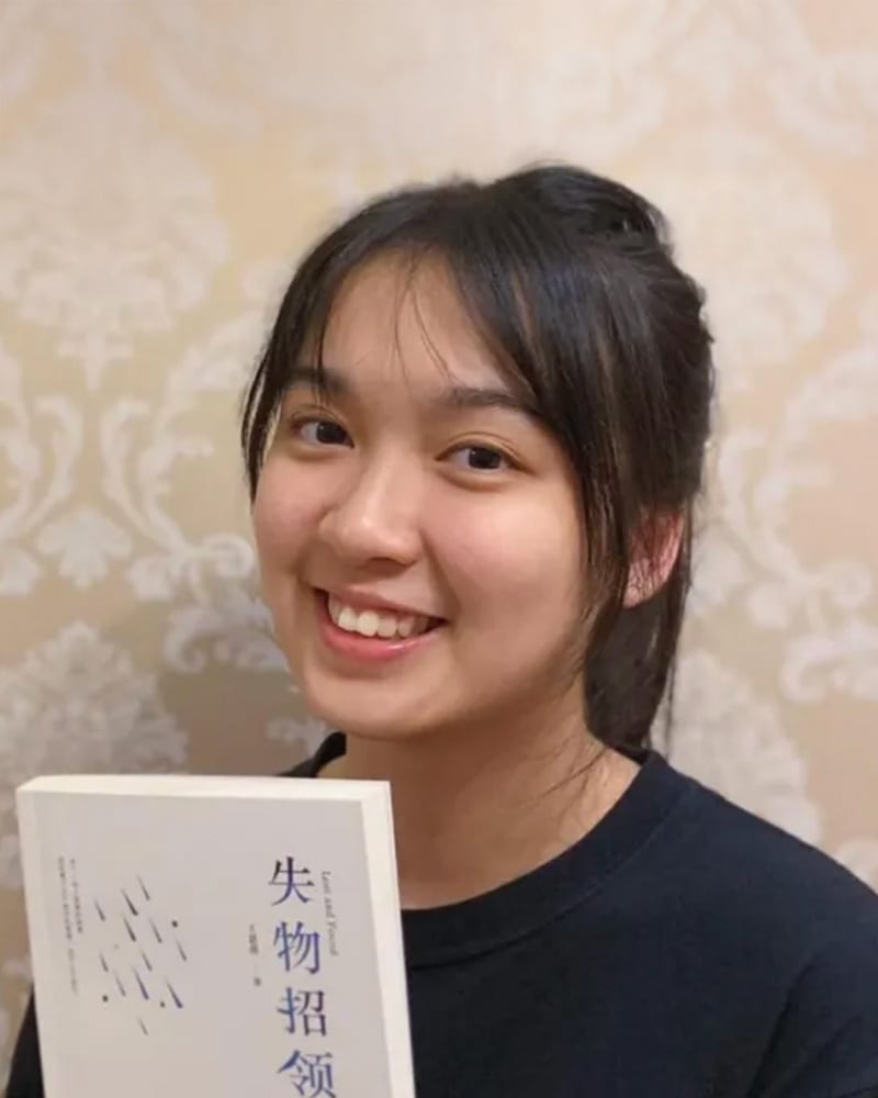 A young woman with dark hair smiles while holding a book titled "Lost and Found" in Chinese characters.