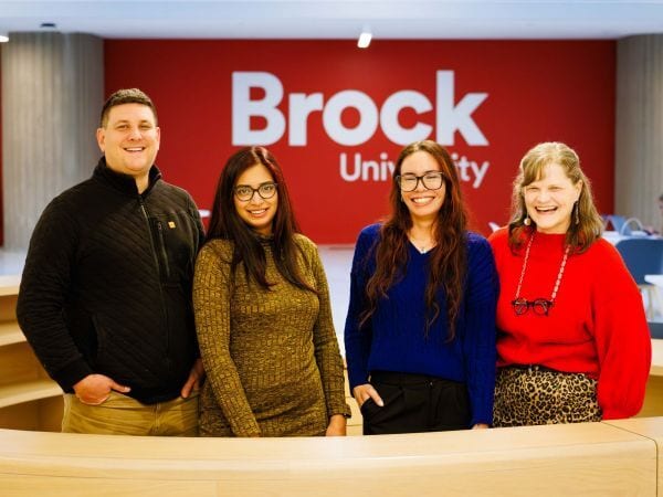 Four smiling people in front of a Brock University sign.