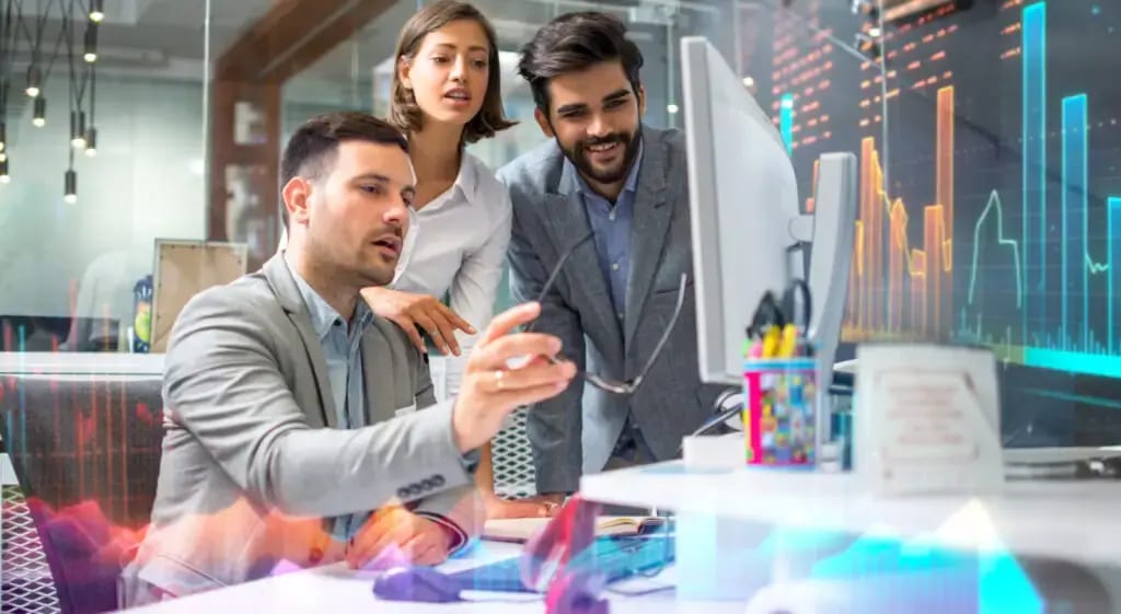 Three business colleagues collaborating on data analysis, looking at graphs on a computer screen.