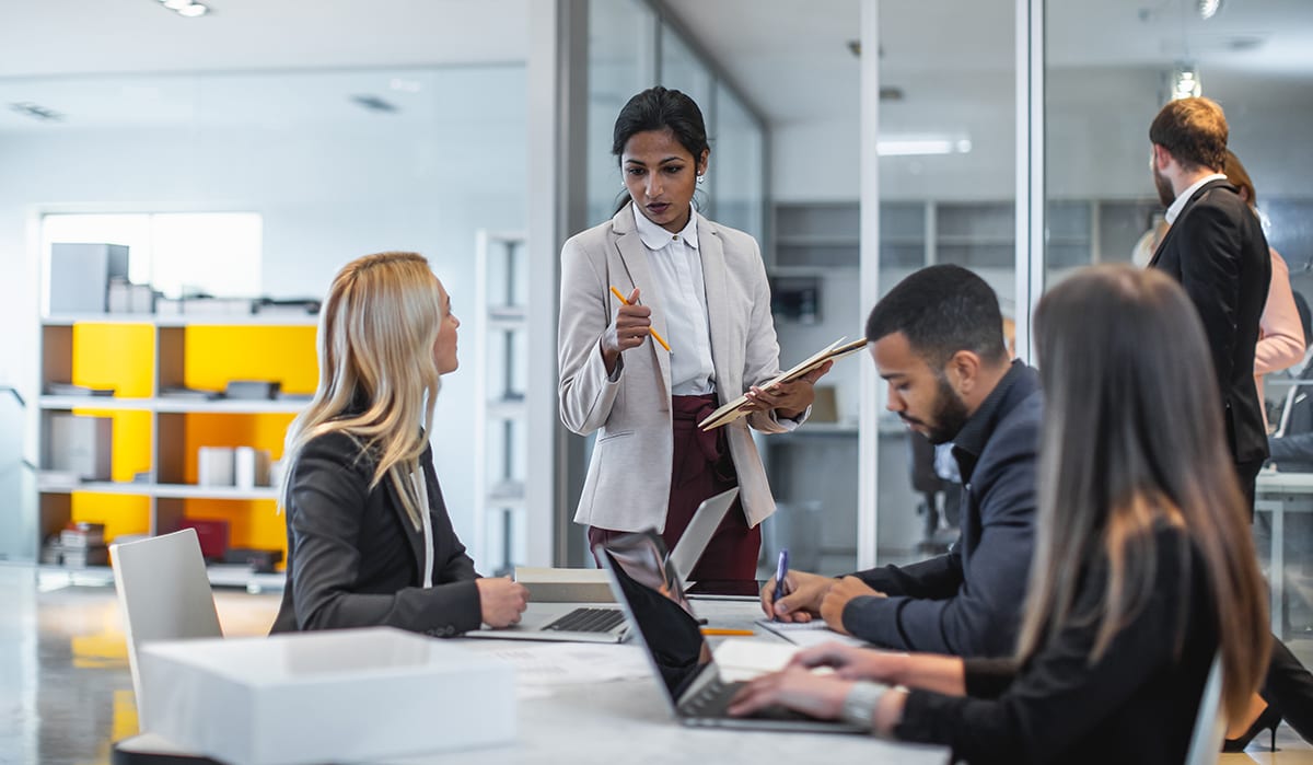 Diverse business people in an office meeting, a woman leads a discussion.