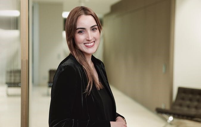 Smiling woman in black jacket, office background.