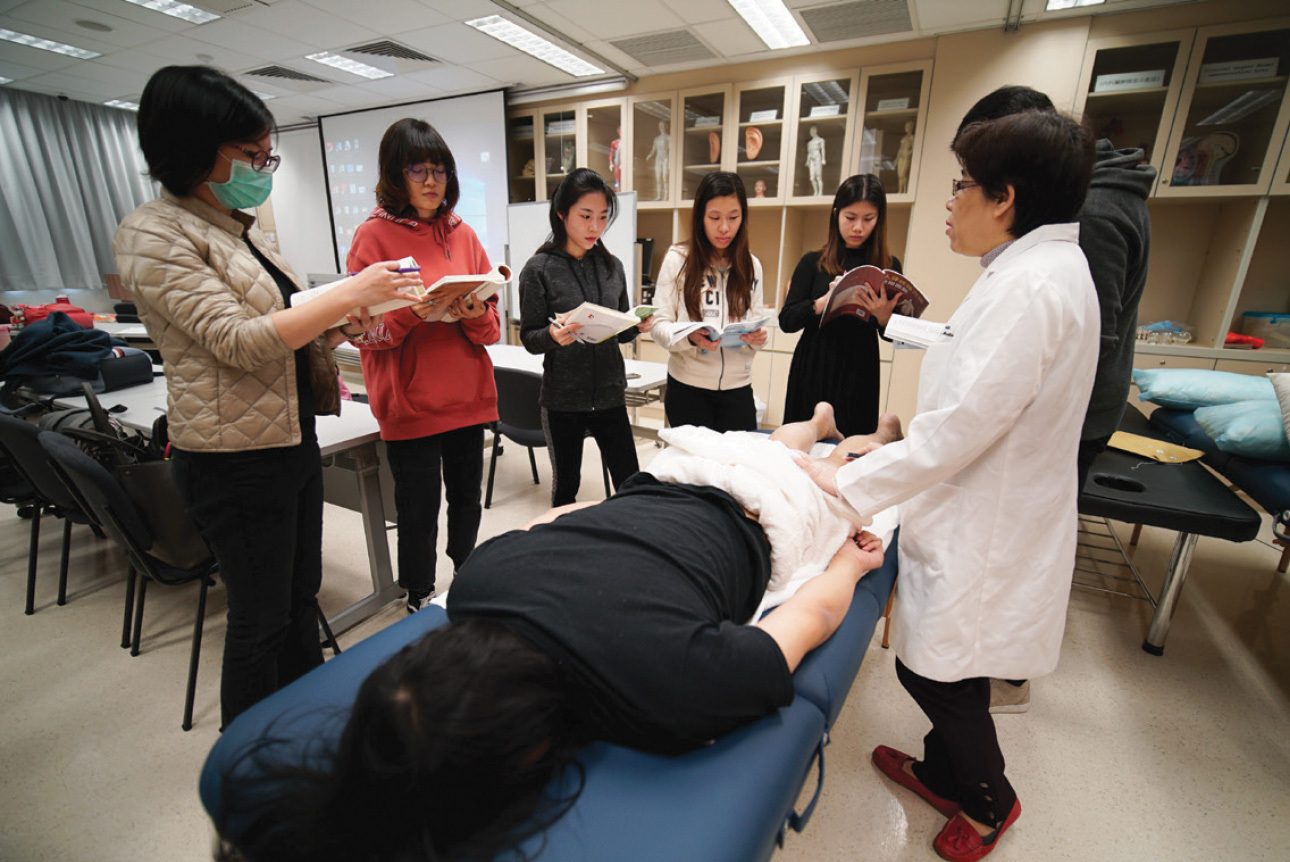 Medical instructor and students examine a patient on a table in a classroom.