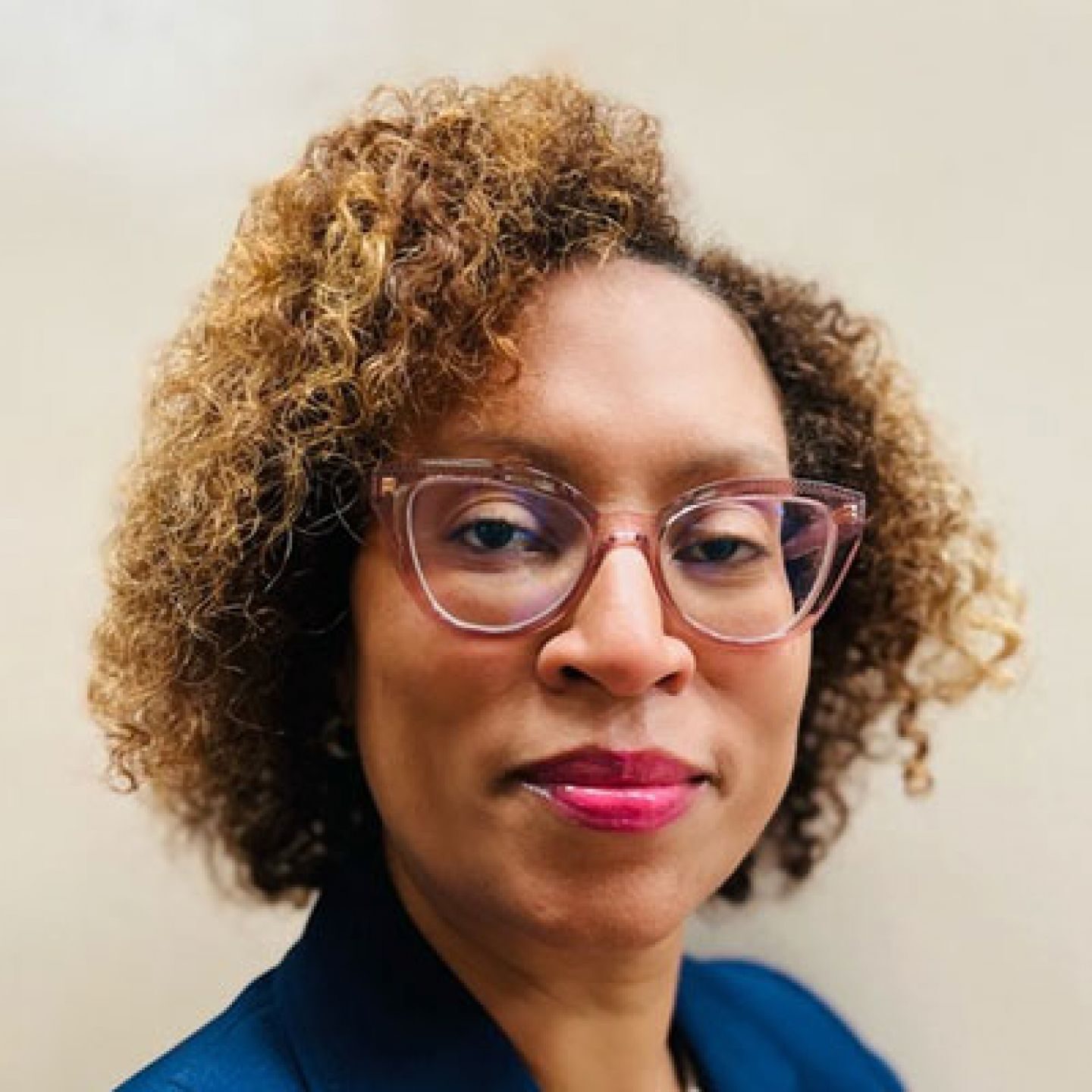 Headshot of a woman with curly hair, pink cat-eye glasses, and a blue top.