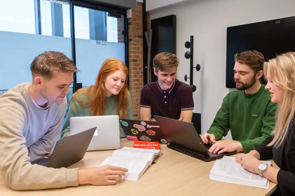 Five young people studying together around a table with laptops and books.