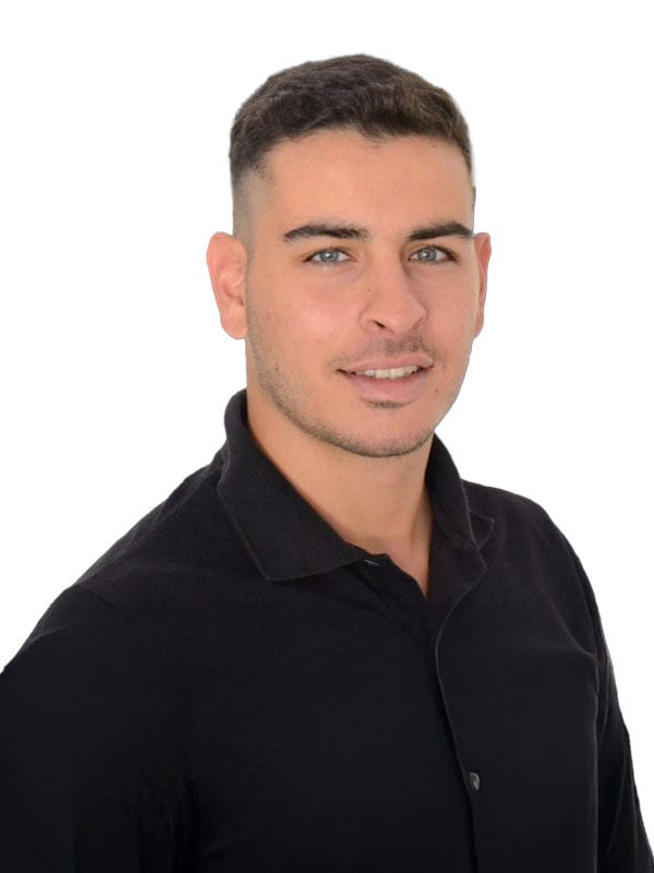Headshot of a smiling man with short dark hair and light eyes, wearing a black collared shirt.