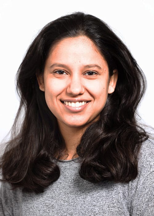 Smiling woman with long dark hair in a grey top, white background.