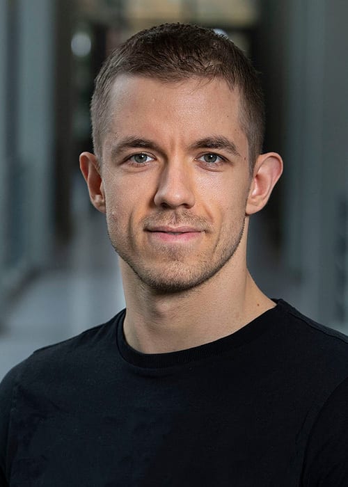Headshot of smiling man with short dark hair, light eyes, and black t-shirt.