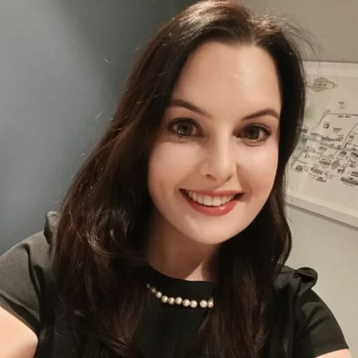 Smiling woman with dark hair wearing a black top and pearl necklace.