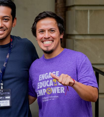 Smiling man in purple 'College of Education' shirt giving thumbs up.