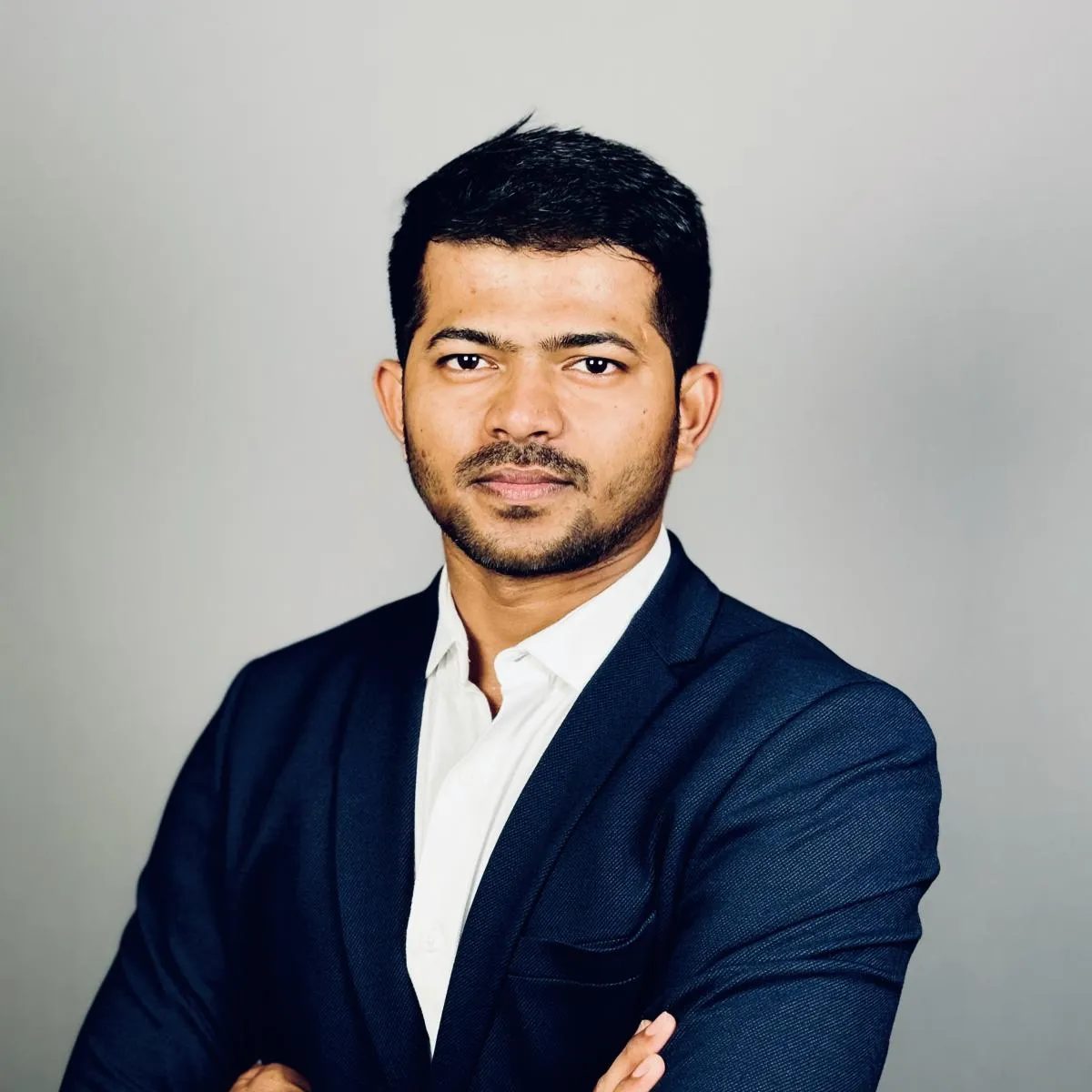 Man in dark suit, white shirt, with beard, arms crossed, looking at camera.